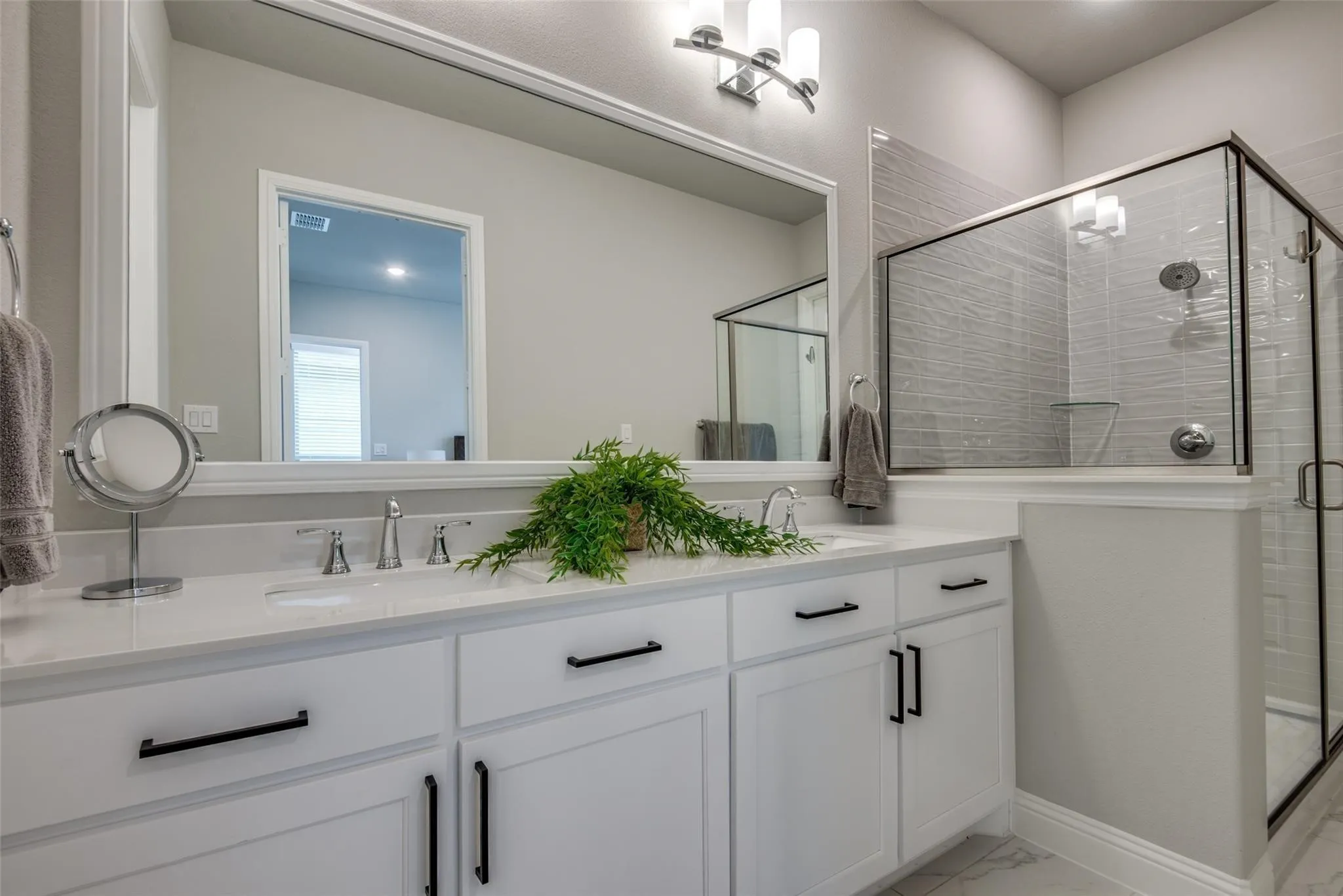 Double vanity with white cabinetry, matte black hardware, and an expansive mirror
