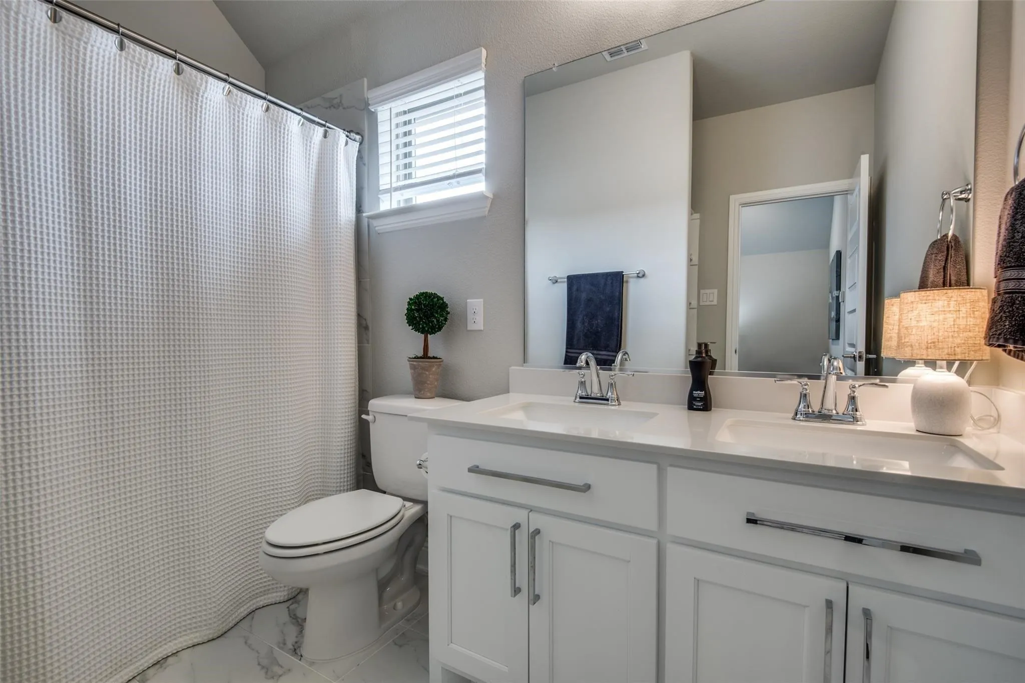 Spa-inspired primary bathroom featuring a dual-sink vanity with white cabinetry, polished countertops, and chrome fixtures
