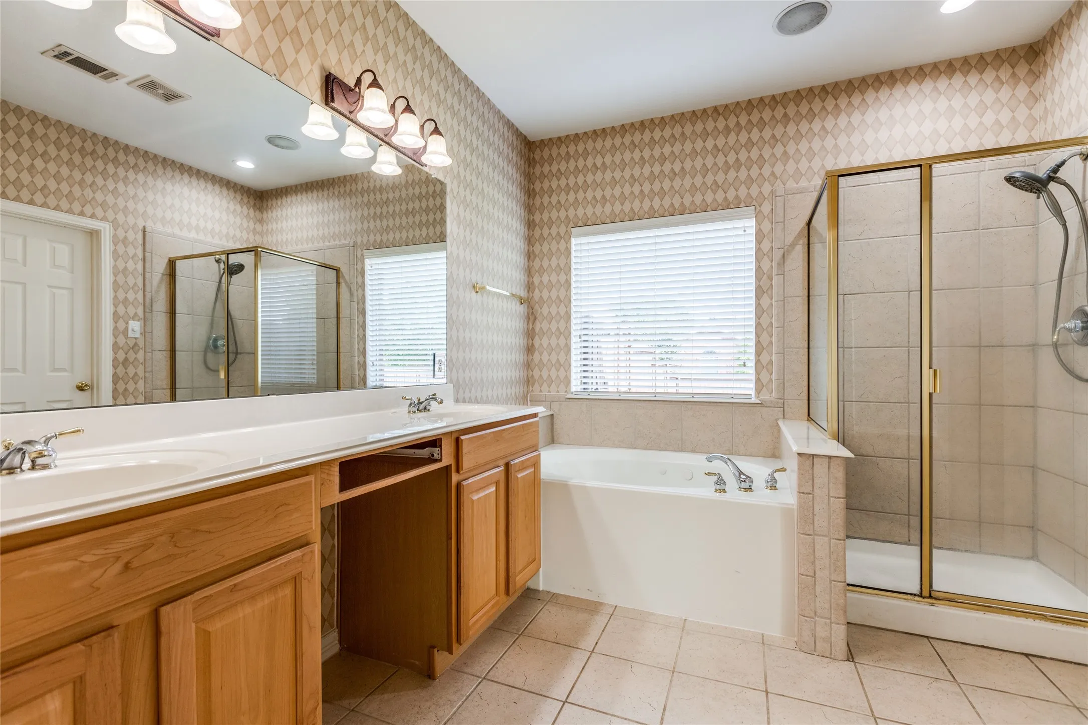 Spa-inspired master bathroom featuring dual vanity with wood cabinetry and ample countertop space, large soaker tub positioned beneath a transom window, walk-in shower with frameless glass enclosure and tile surround, recessed lighting, and neutral tile flooring throughout