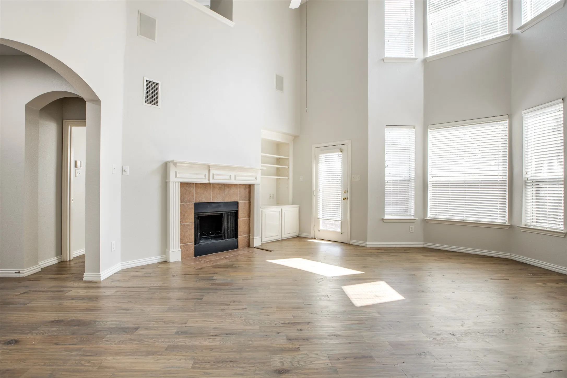 Spacious great room showcasing soaring ceilings with clerestory windows, wood-finish flooring throughout, and a brick fireplace with dark surround