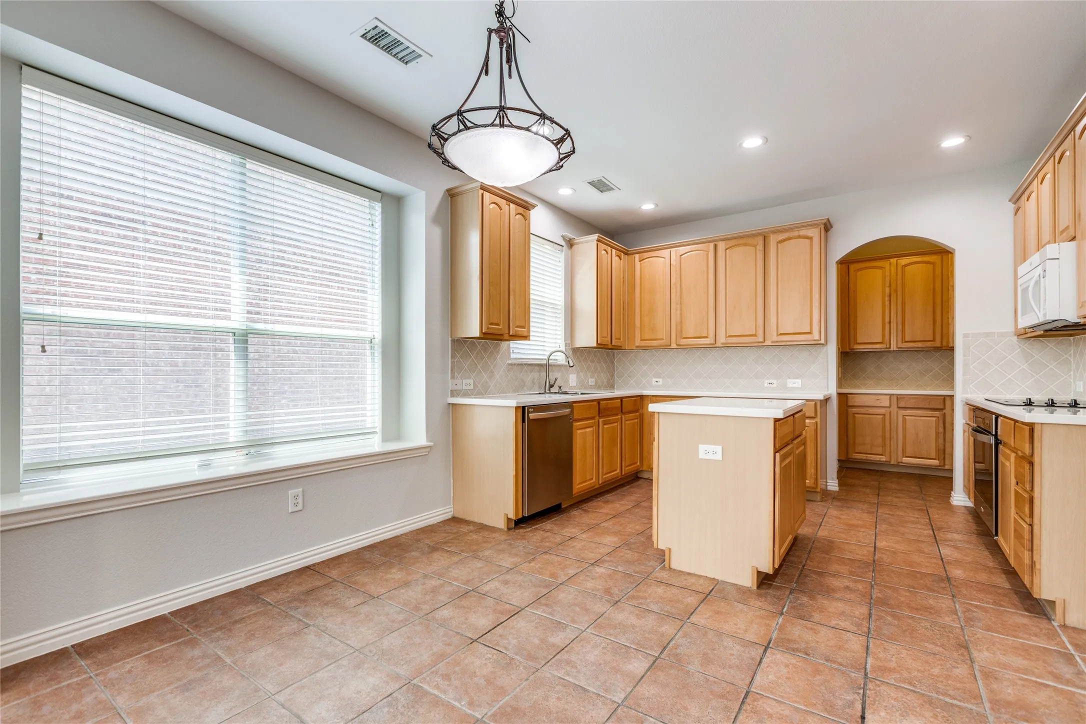 Spacious kitchen featuring wood-finish cabinetry, tile flooring, a central island with prep space, large windows with natural light, and a doorway opening to additional living areas