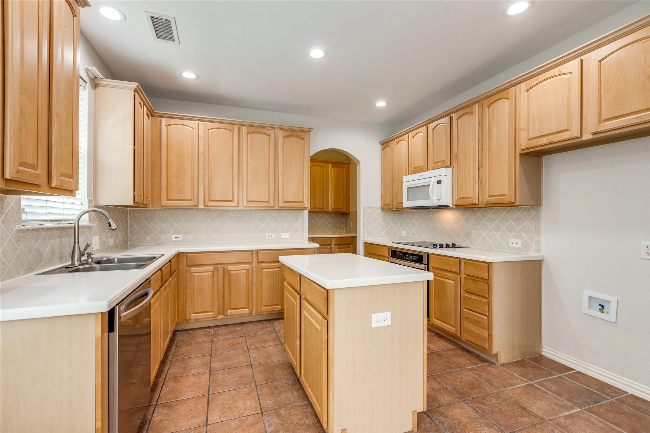 Spacious kitchen featuring warm wood cabinetry throughout, white countertops, tile flooring, a center island with additional counter space, stainless steel appliances, recessed lighting, and a convenient pass-through opening to an adjacent room