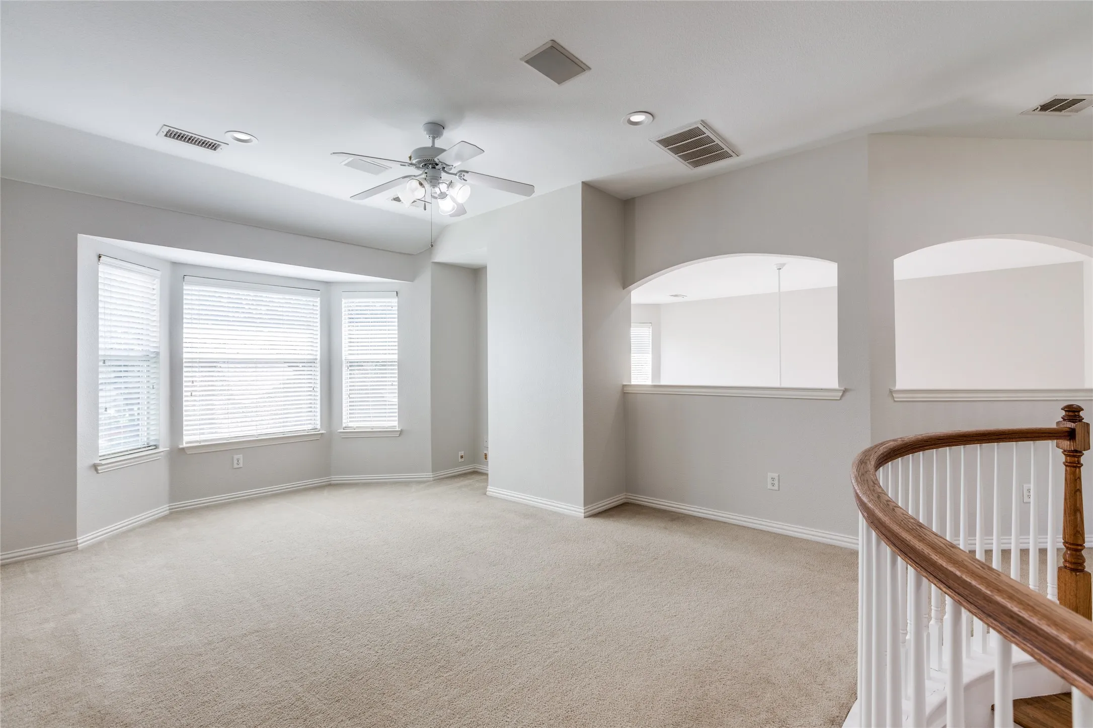 Spacious upper-level room featuring pristine beige carpet, recessed ceiling lighting, and a ceiling fan