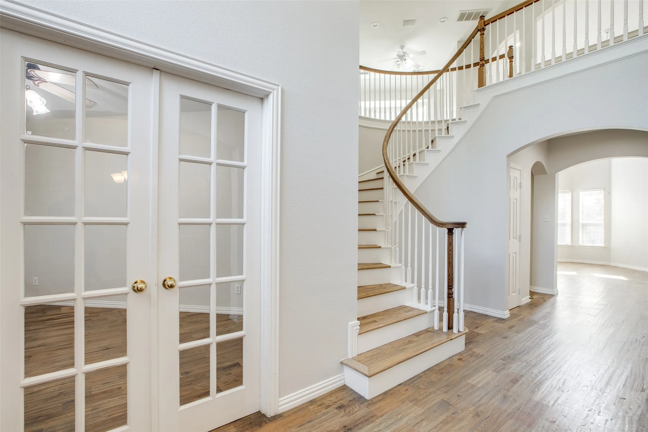 Elegant foyer showcasing a curved staircase with wood treads and brass railings, gleaming wood-finish flooring, and French doors with multiple glass panes leading to adjacent spaces