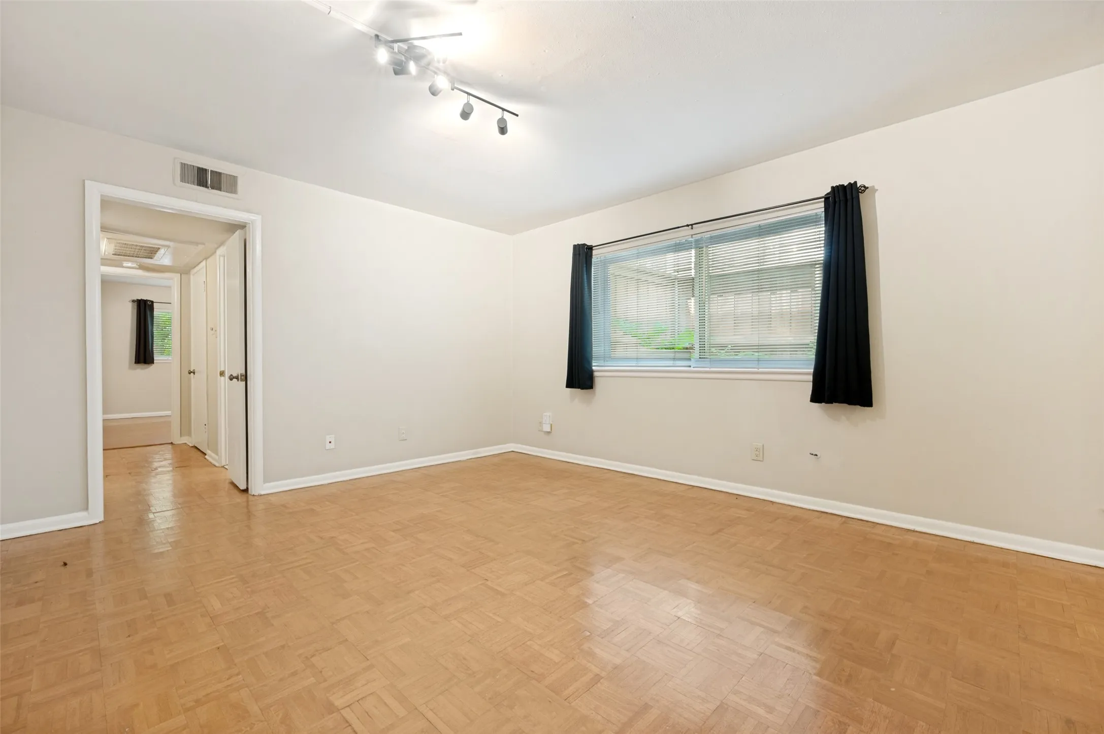 Spacious interior room featuring parquet wood flooring, white baseboards, and neutral wall paint