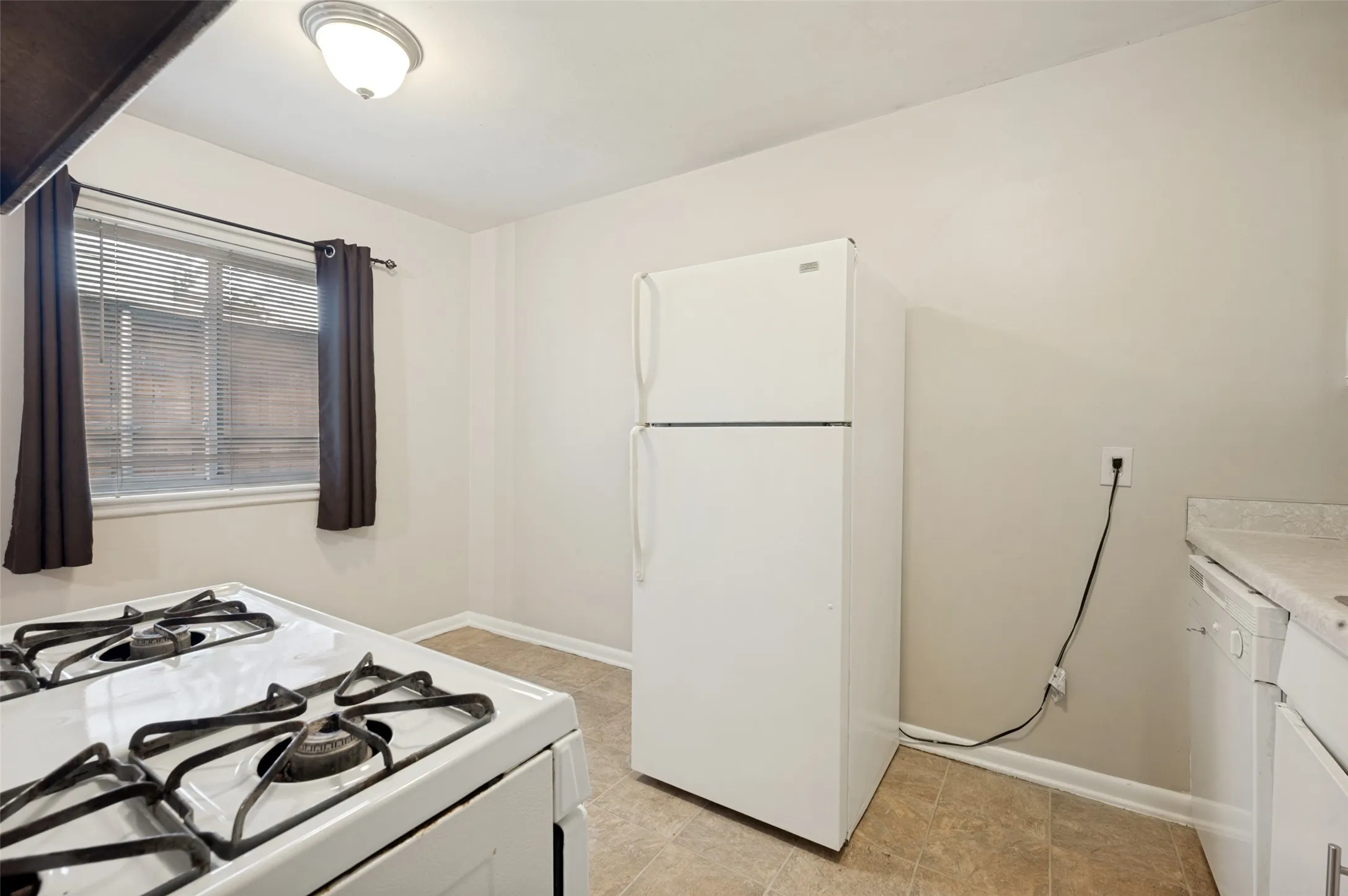 Efficient kitchen featuring a gas cooktop with multiple burners, white refrigerator with freezer compartment, and ceramic tile flooring