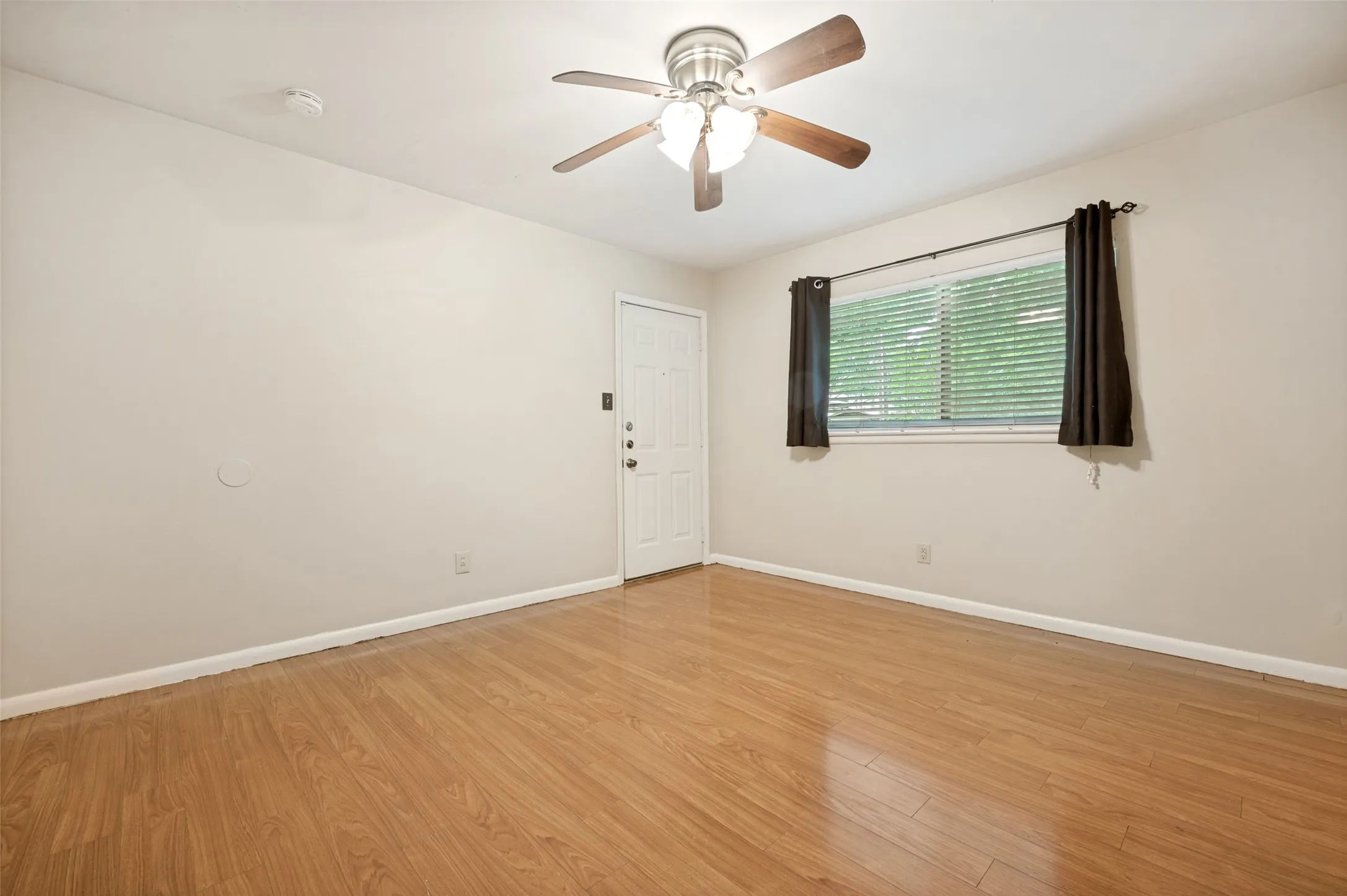 Room featuring wood-finish flooring, a ceiling fan with integrated lighting, and a white entry door