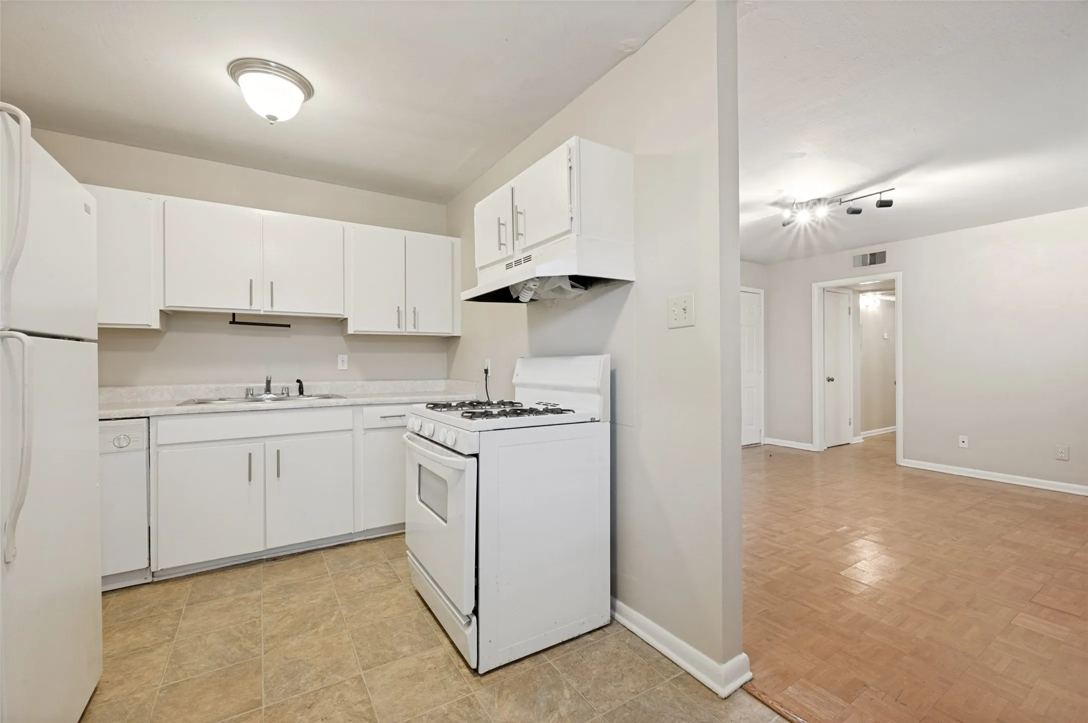 Bright, open kitchen featuring white cabinetry, stainless steel gas range with overhead hood, white refrigerator, and ample counter space