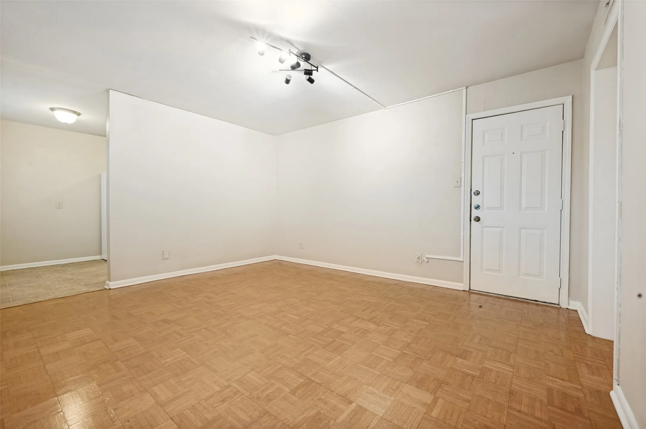 Spacious open room featuring herringbone wood-finish flooring, white painted walls, recessed lighting, and a white six-panel entry door