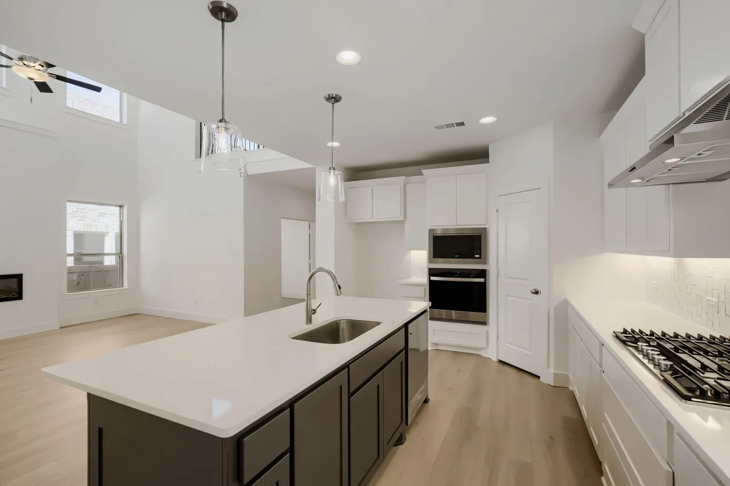 Open-concept kitchen featuring an island with a stainless steel sink, white cabinetry, integrated stainless steel appliances, and wood-finish flooring
