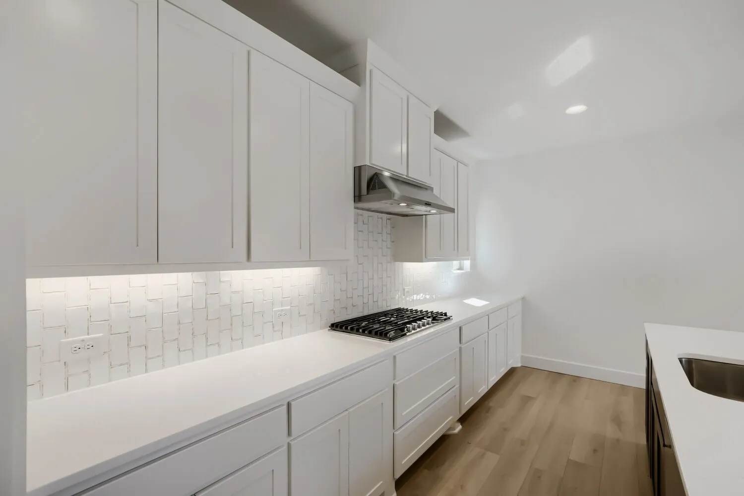 White shaker cabinetry, quartz countertops, tile backsplash, built-in gas range, and wood-finish flooring