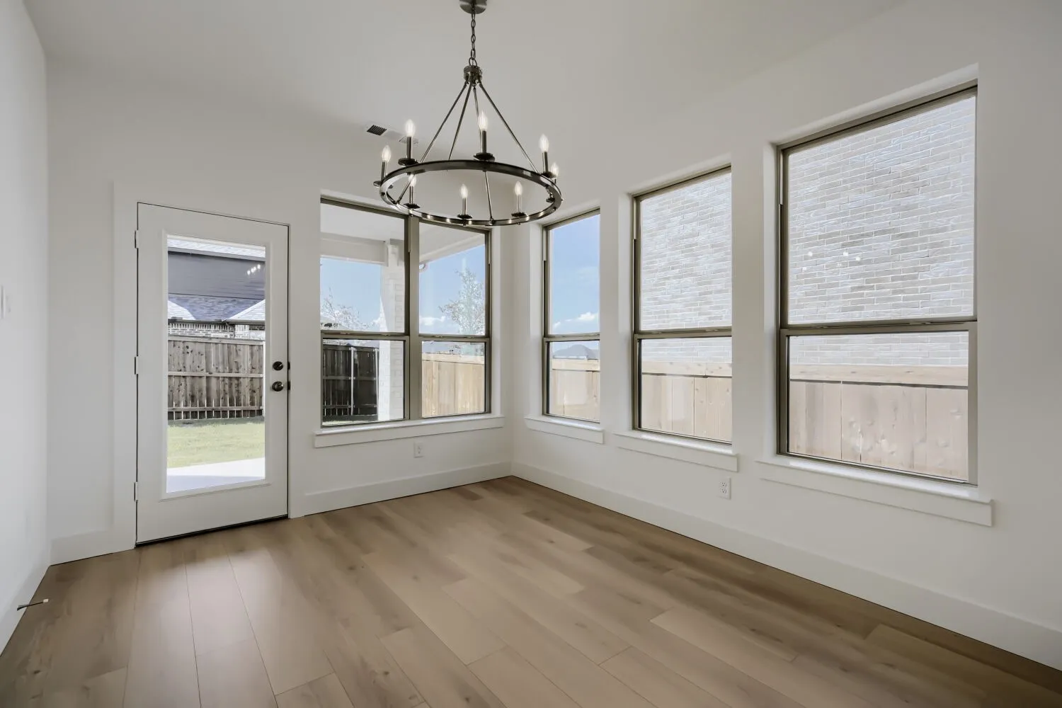 Light wood-finish flooring, a contemporary chandelier, multiple windows, and a glass-paneled exterior door
