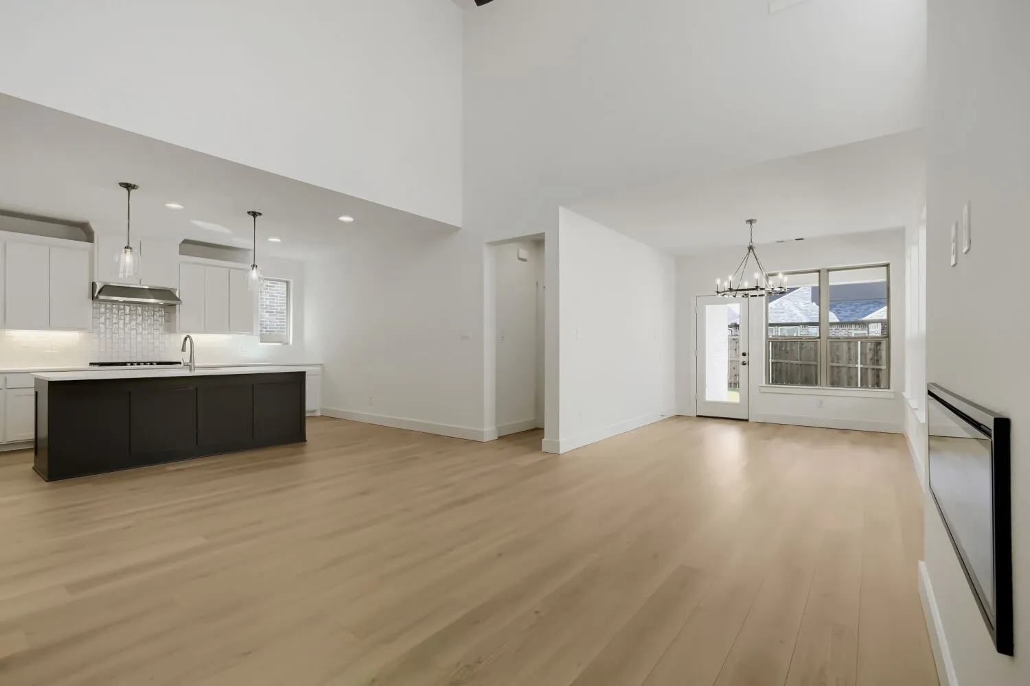 High ceilings with recessed lighting, light wood-finish flooring, and a kitchen featuring white cabinetry, a dark island, and pendant lighting