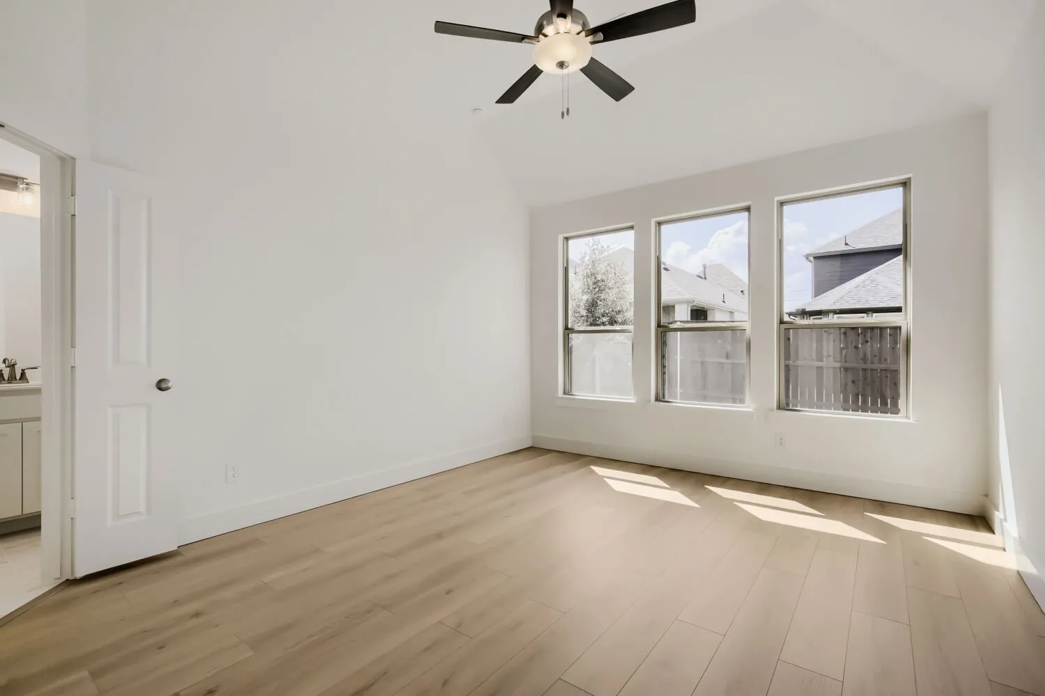 Vaulted ceiling with a ceiling fan, three large windows, and wood-finish flooring