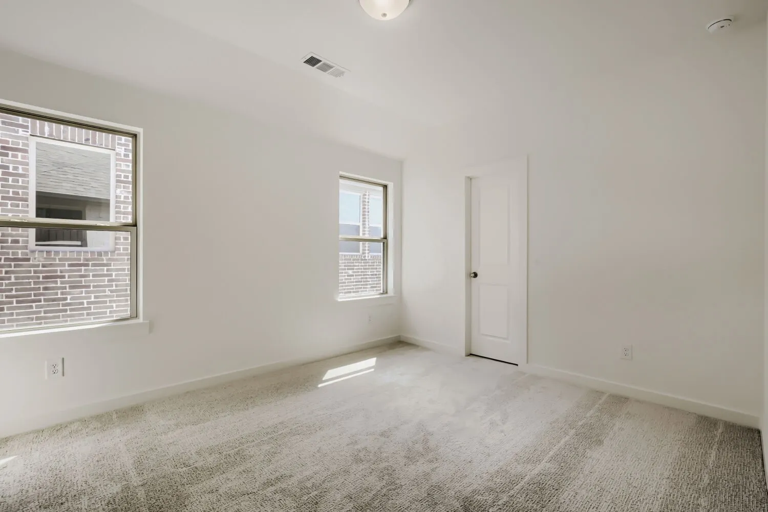 White walls, light-toned carpet flooring, two windows, and a white interior door