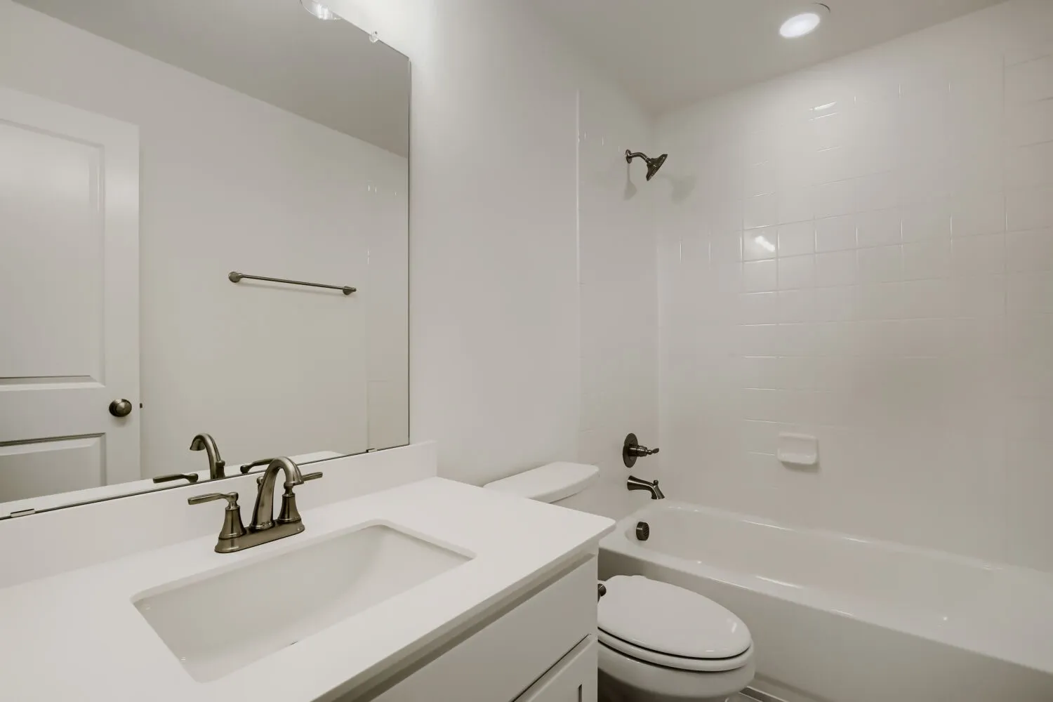 Bathroom featuring a white vanity with an integrated sink, bronze-finish faucet, and a bathtub with white subway tile surround