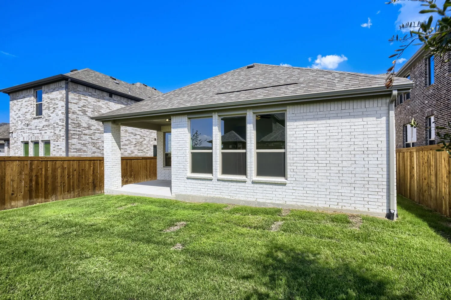Manicured lawn with a covered patio, brick exterior, and a wood privacy fence