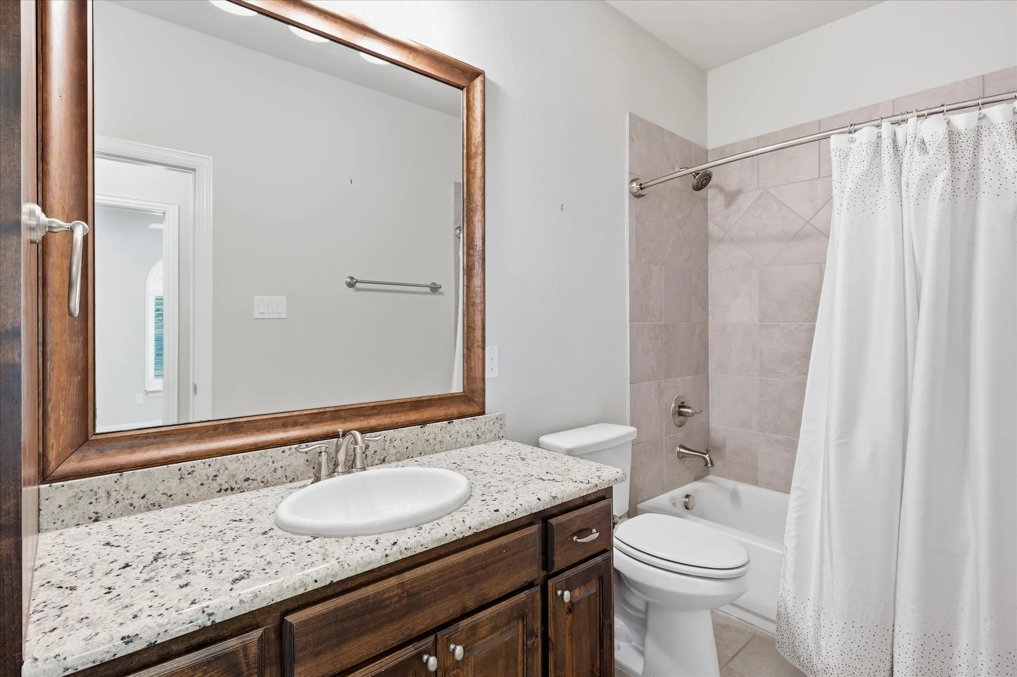 Bathroom featuring a wood-framed mirror, granite-look countertop, wood-finish vanity, and a tiled tub/shower combination