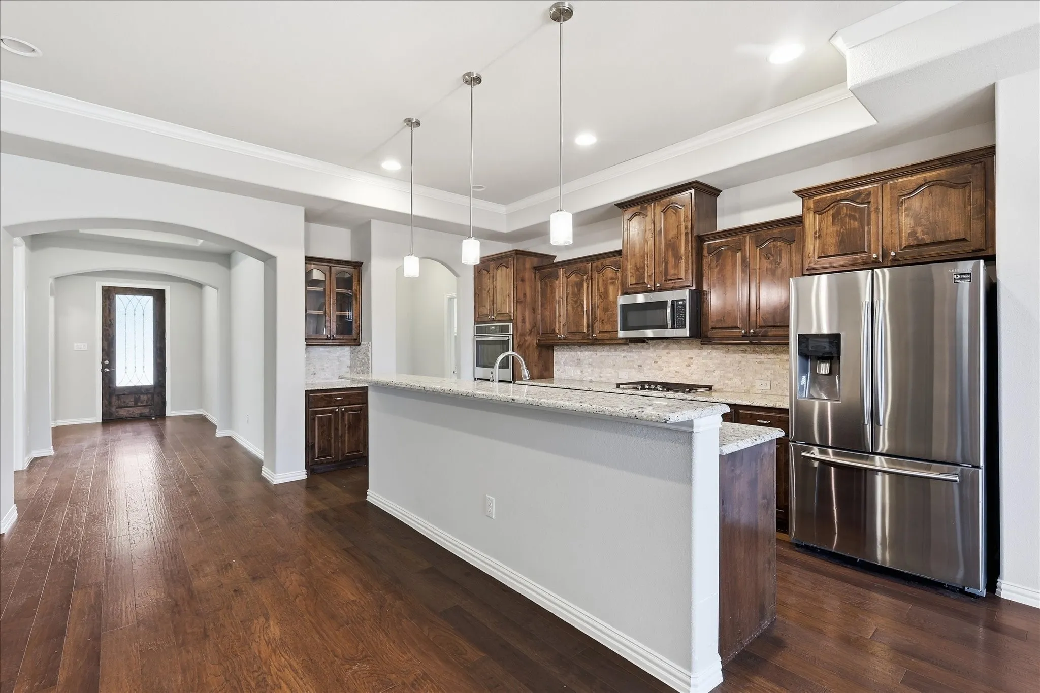 Kitchen featuring rich wood cabinetry, stainless steel appliances, a granite countertop island, and pendant lighting