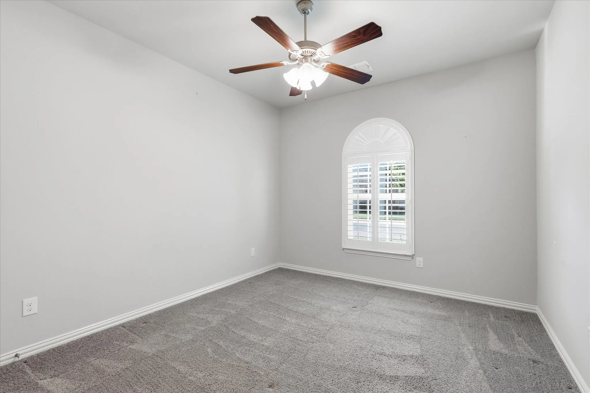 Carpeted room featuring a ceiling fan with wood-finish blades, a vaulted ceiling, and an arched window with plantation shutters