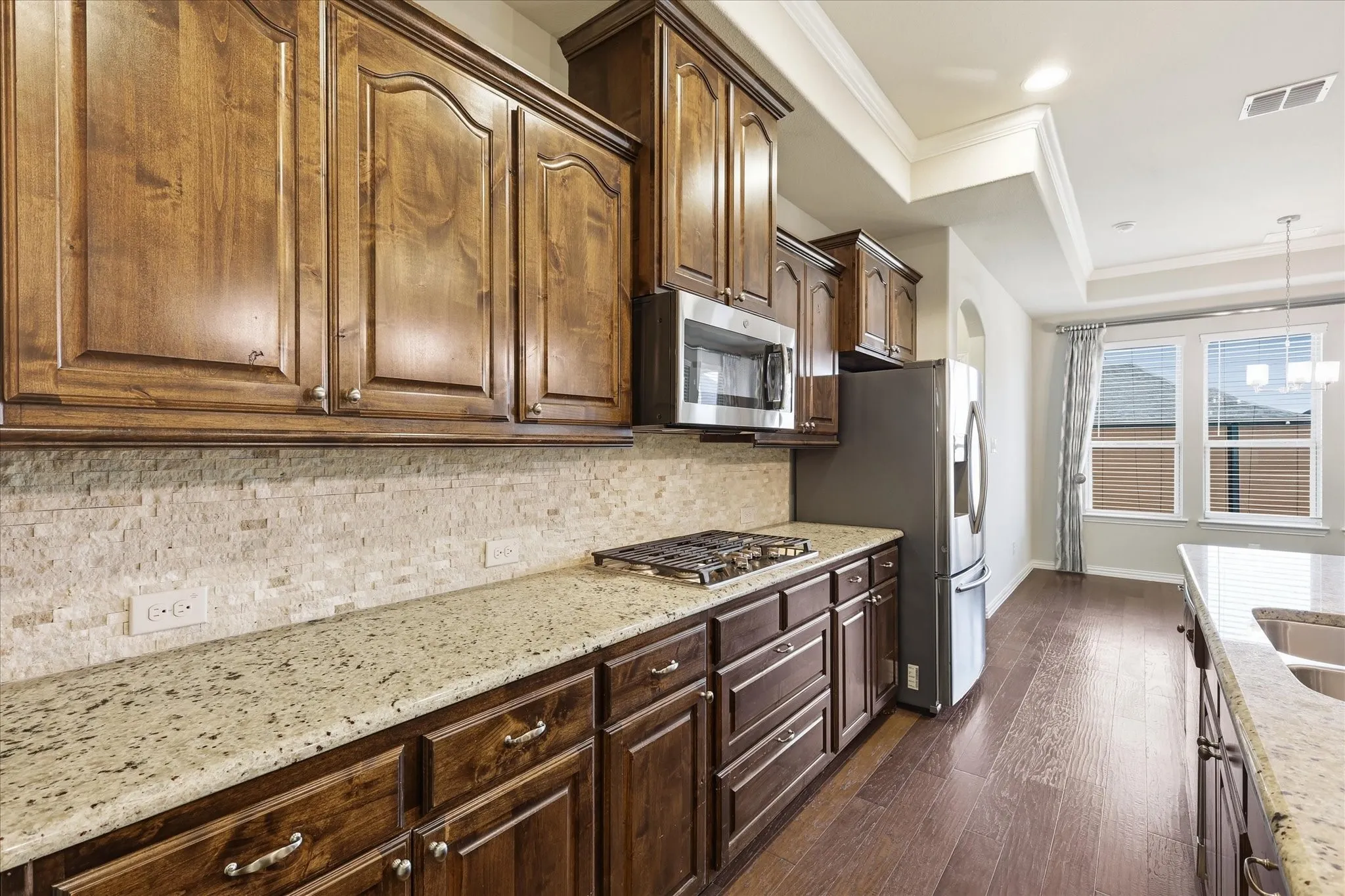 Kitchen featuring rich wood cabinetry, light-toned granite countertops, a tiled backsplash, and stainless steel appliances