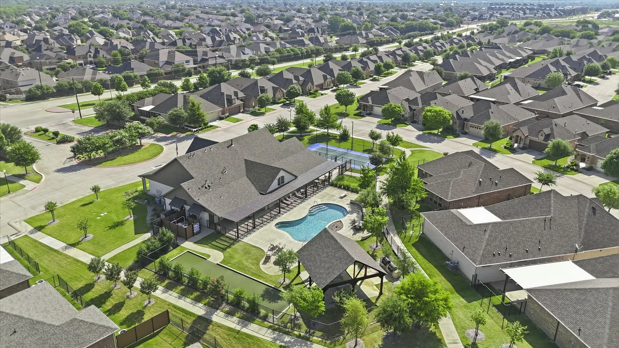 Community amenities featuring a central clubhouse, an outdoor swimming pool, a covered patio area, a sports court, and a bocce ball court