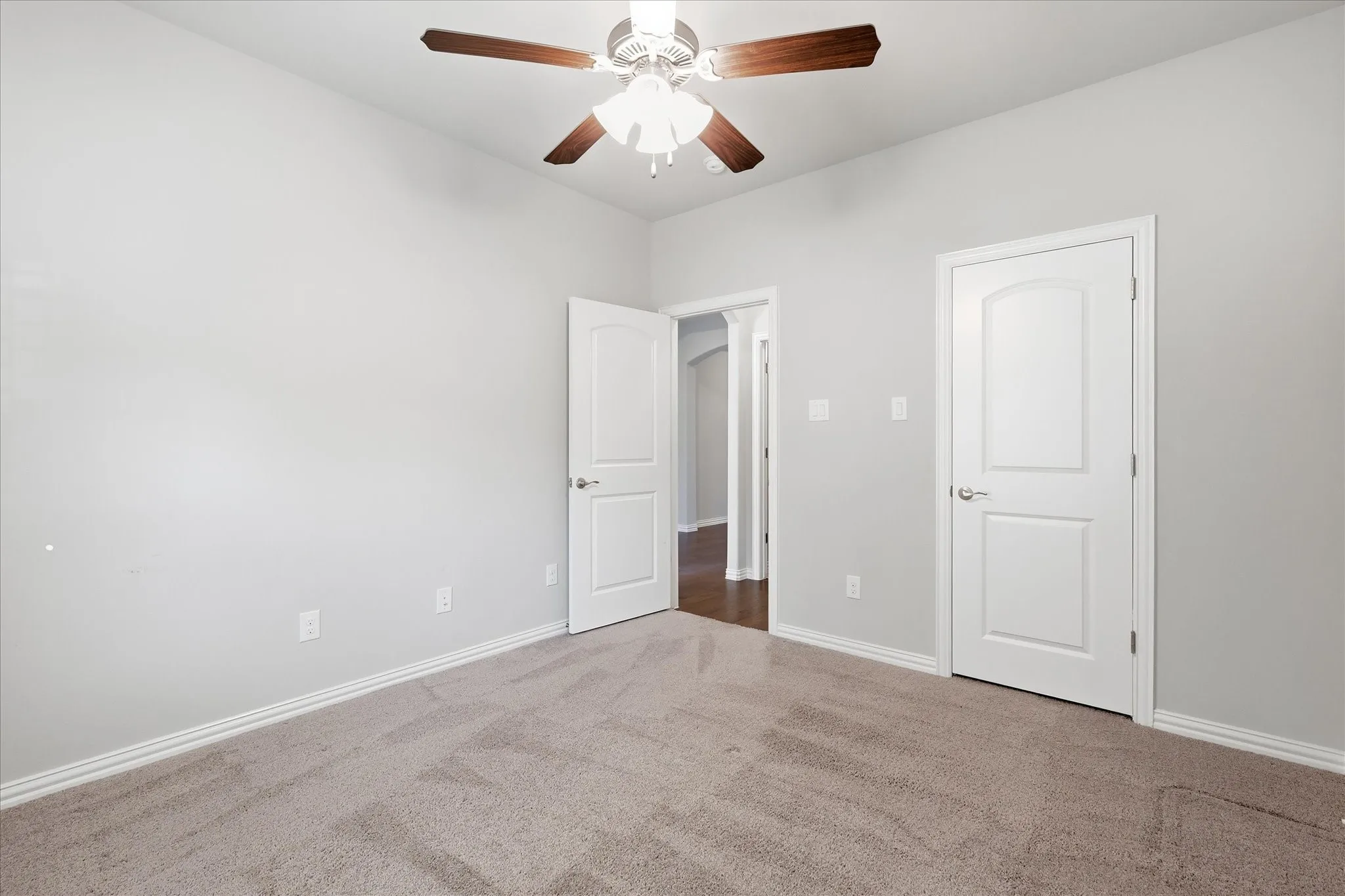 Carpeted interior space featuring light-colored walls and a ceiling fan with wood-finish blades
