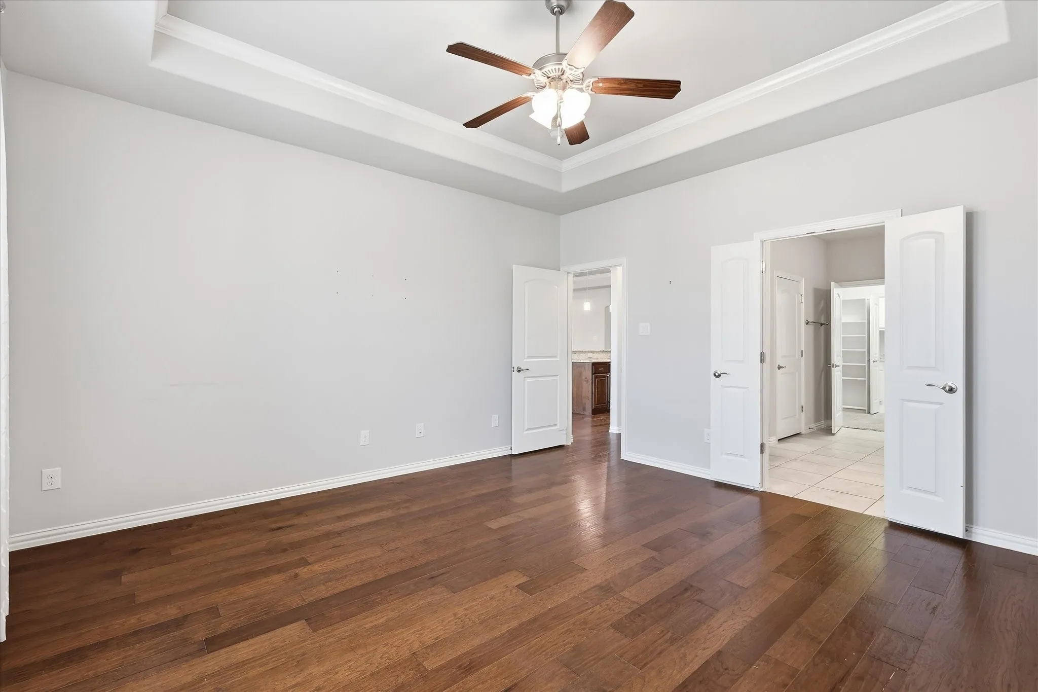 Spacious primary room featuring wood-finish flooring, a tray ceiling, and a ceiling fan