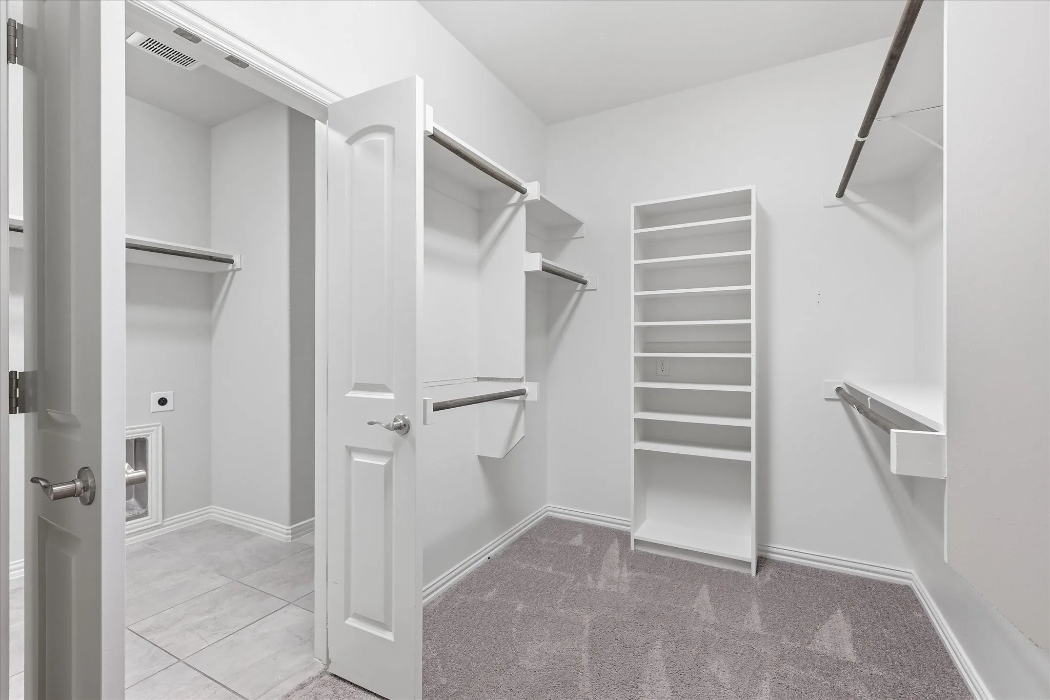 Spacious closet featuring built-in shelving, hanging rods, and plush carpeting that opens to the directly to the laundry room