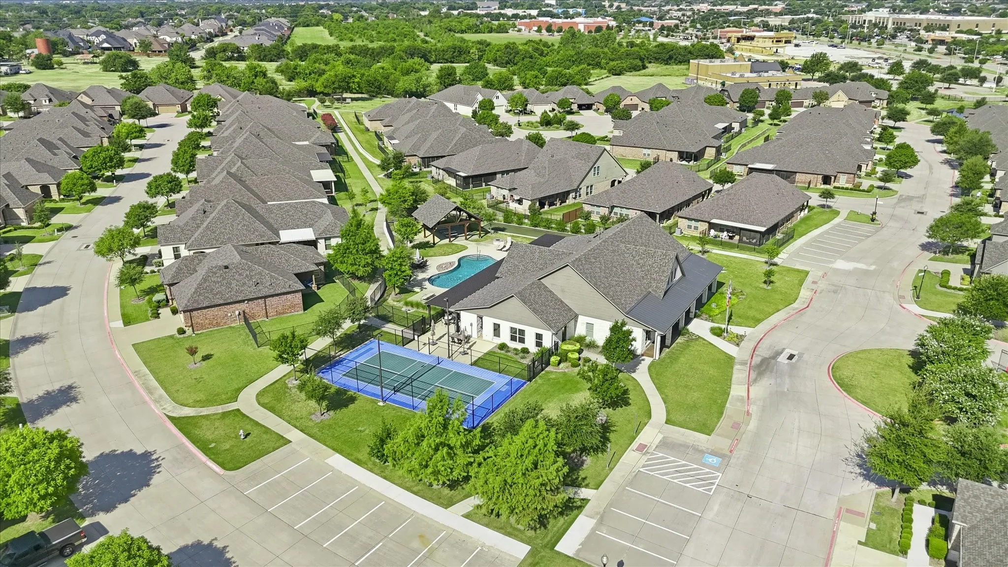 Community recreation area featuring a swimming pool, tennis court, and surrounding residences with manicured lawns