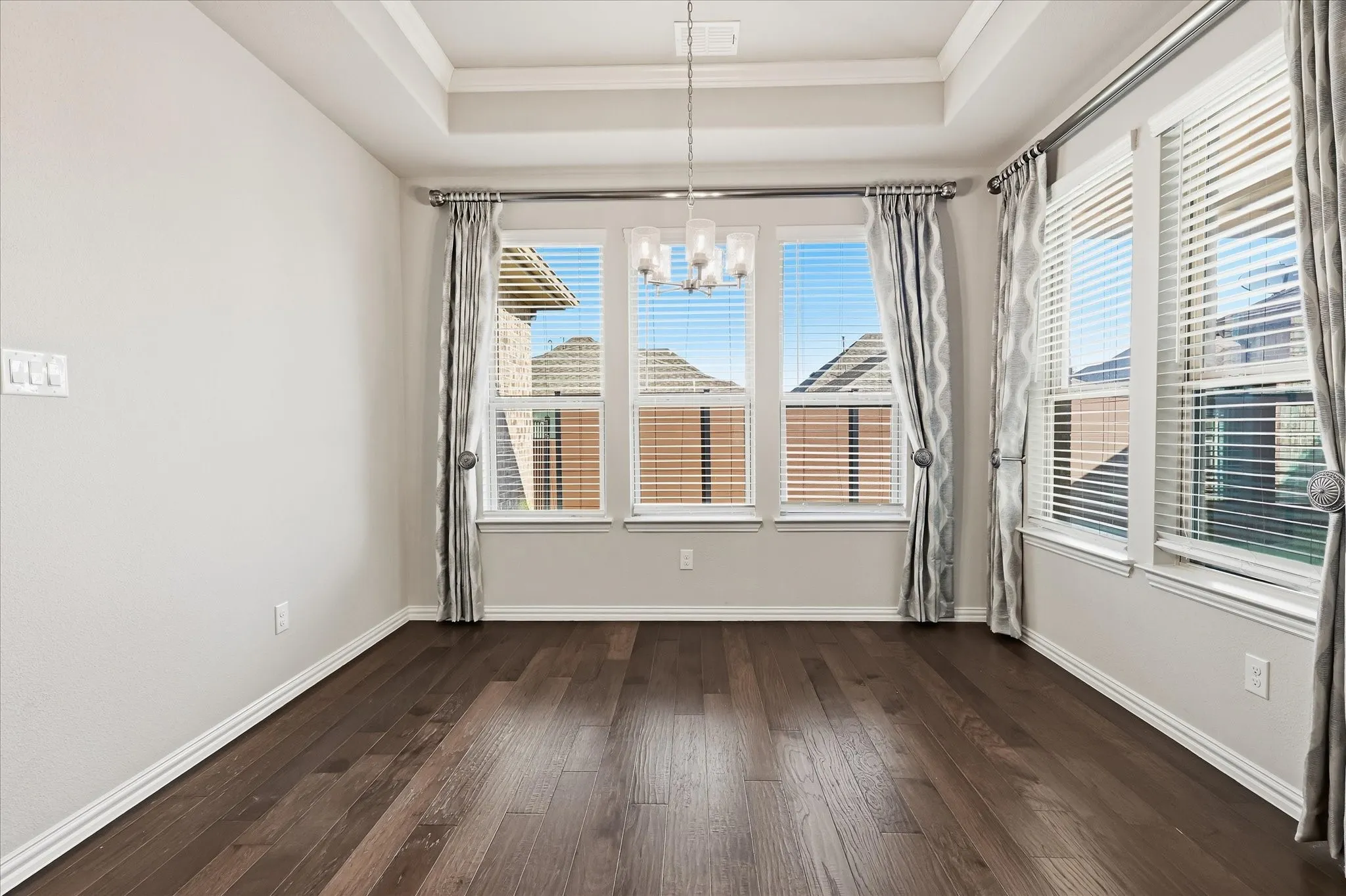 Spacious room featuring dark wood-finish flooring, a tray ceiling, and multiple windows with blinds