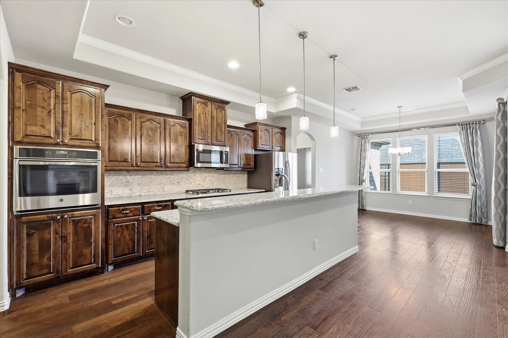 Open-concept kitchen featuring extensive wood cabinetry, stainless steel appliances, a built-in oven, and a large granite countertop island with pendant lighting