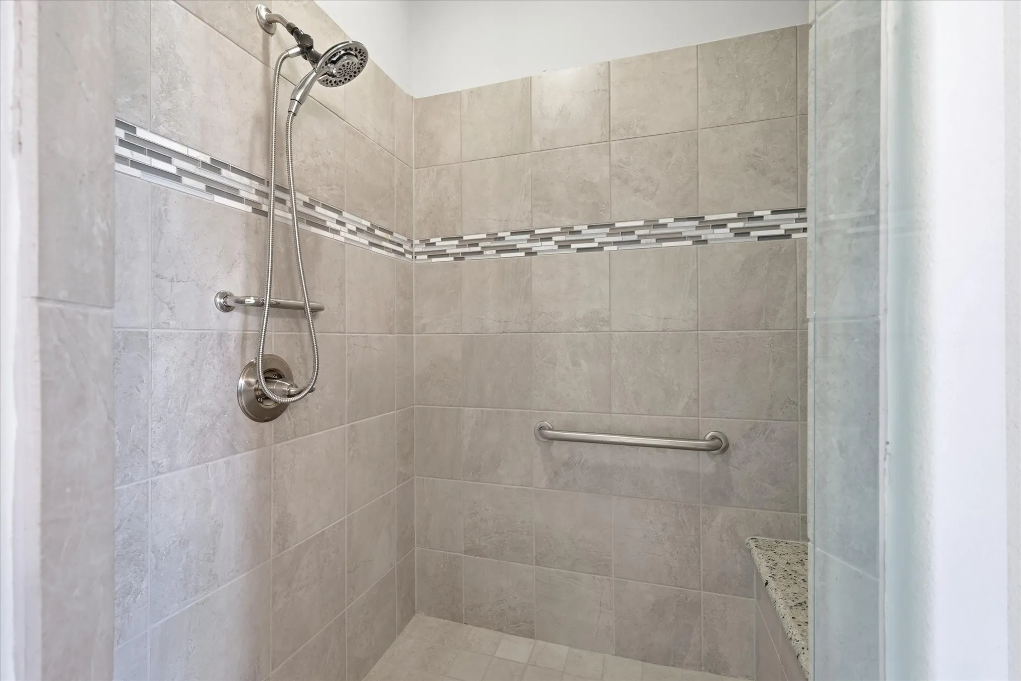 Shower enclosure featuring light-toned tile walls with a decorative mosaic accent band