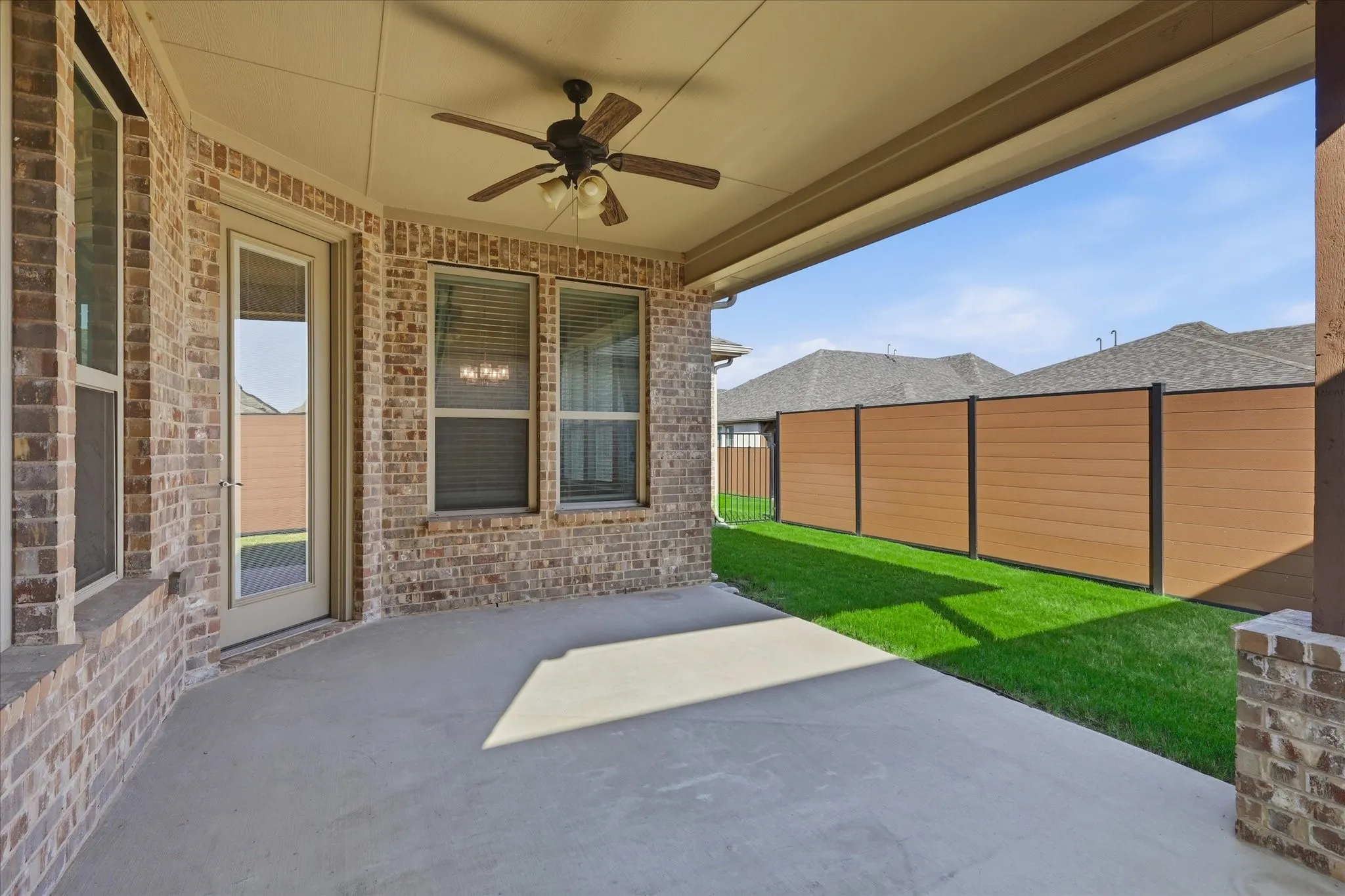 Covered concrete patio with a ceiling fan, brick exterior, and multiple windows