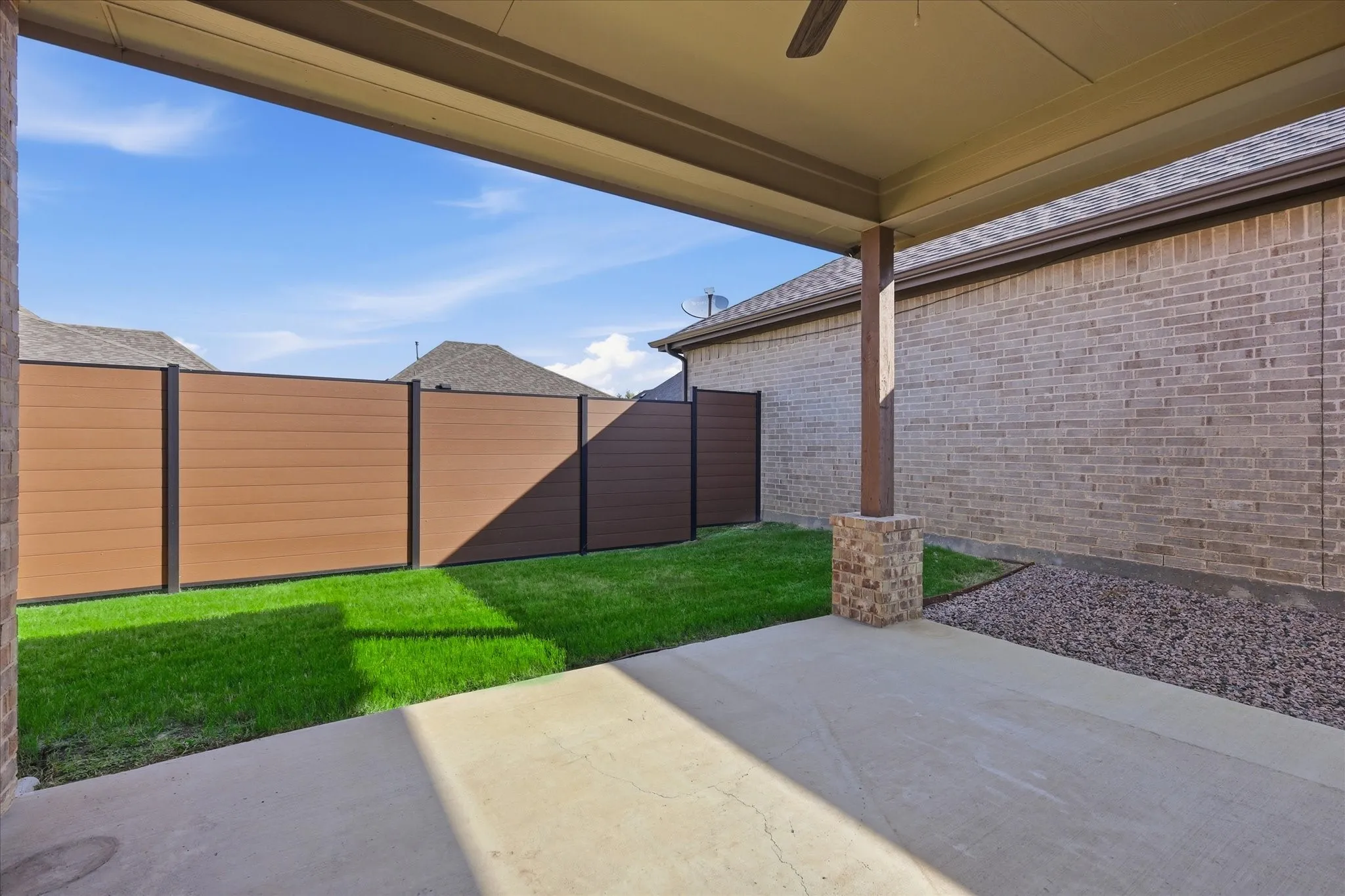 Covered patio featuring a ceiling fan, concrete flooring, and a brick-wrapped support column