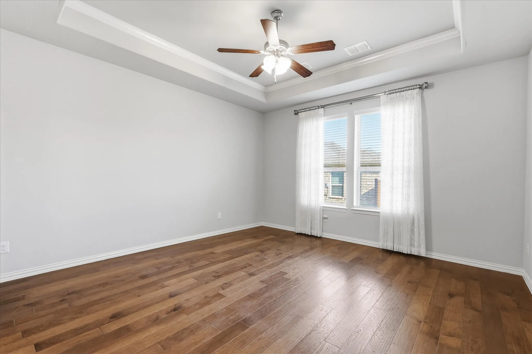Spacious primary room featuring wood-finish flooring, a tray ceiling, and a ceiling fan