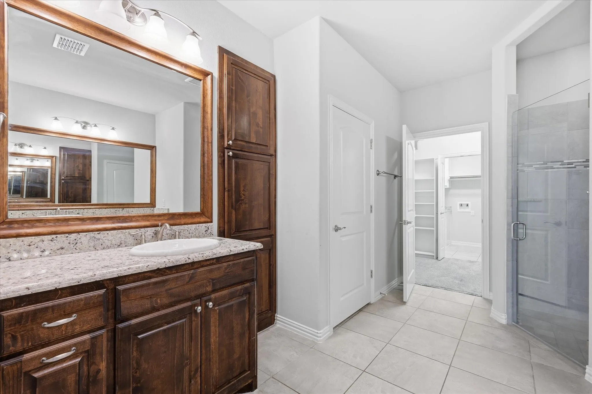 Bathroom featuring a single vanity with a granite-style countertop, dark wood-finish cabinetry, an oval undermount sink, and a framed mirror