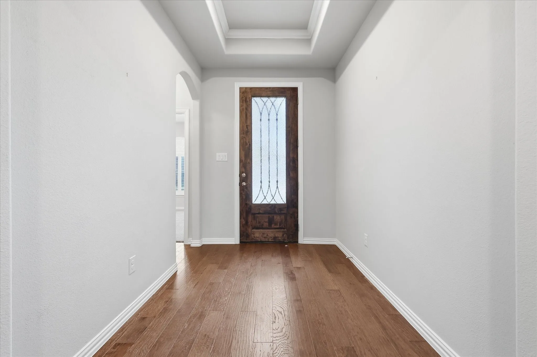 Entryway featuring wood-finish flooring, a tray ceiling with crown molding, and a dark wood door with decorative glass inserts
