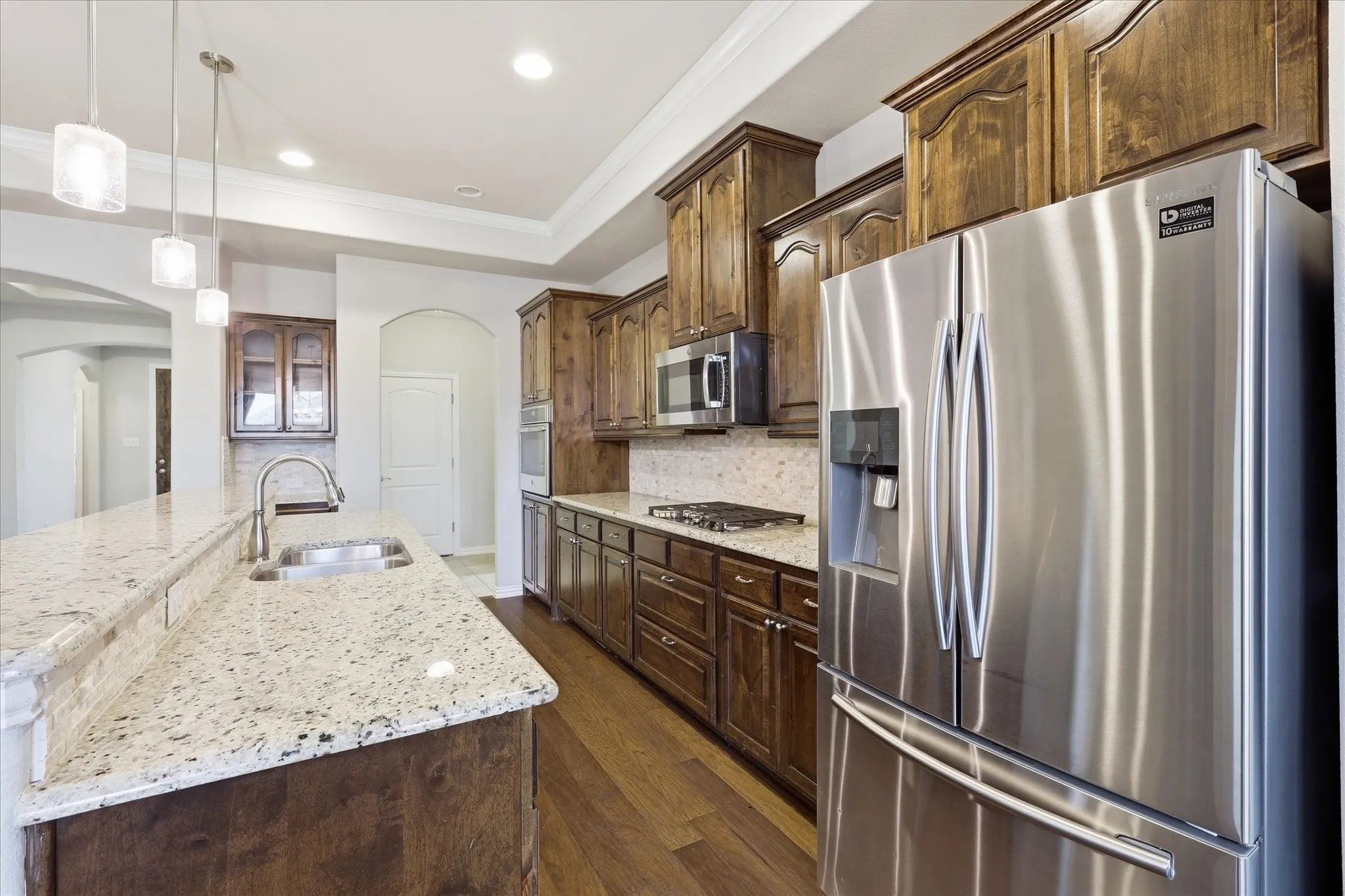 Kitchen featuring a stainless steel refrigerator, dark wood-finish cabinetry, light-toned stone countertops, and wood-finish flooring