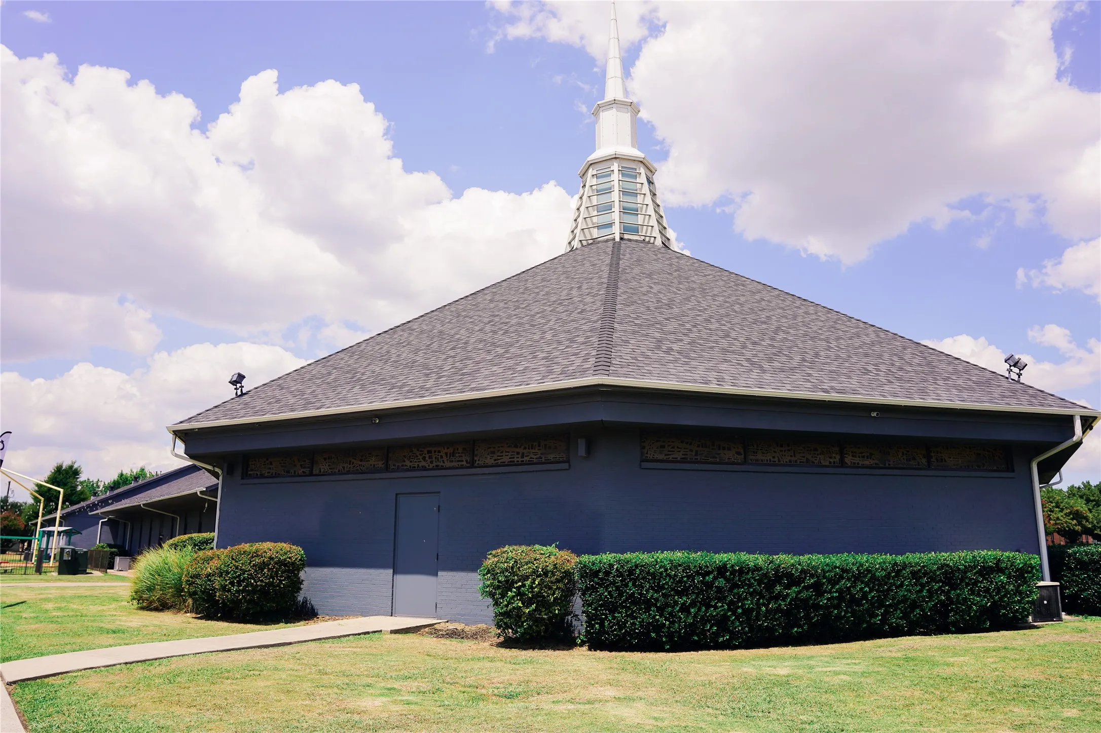 Modern circular architectural design featuring a distinctive domed roof with cupola and spire, complemented by a charcoal gray exterior finish