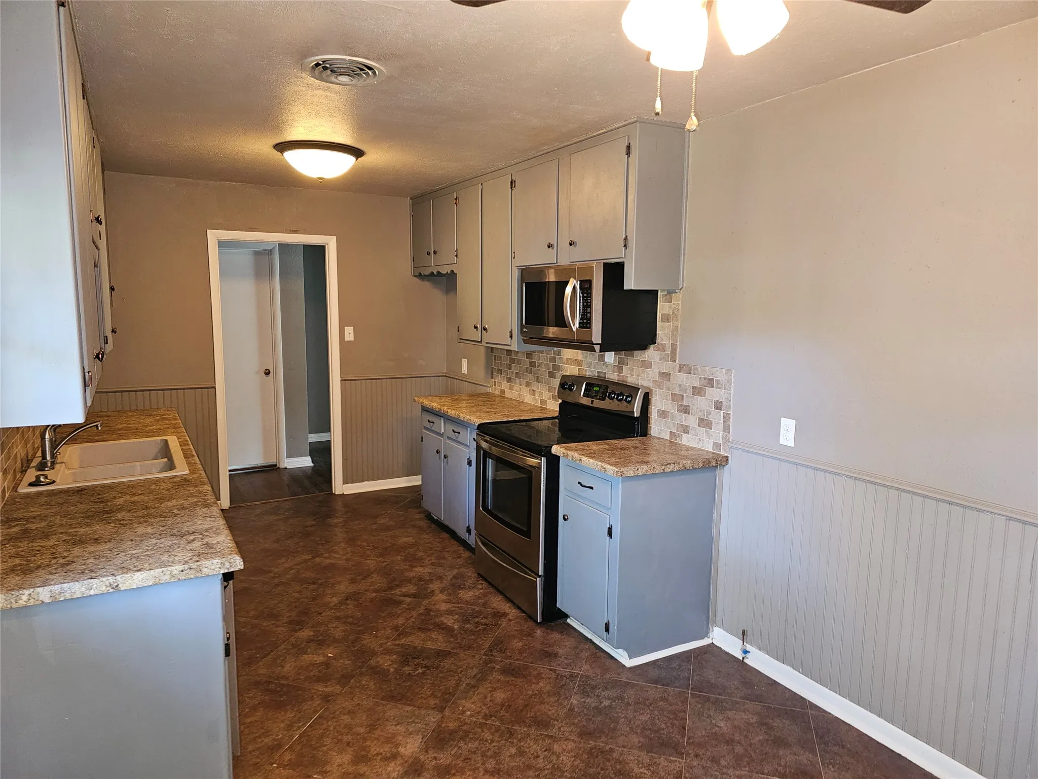 Kitchen featuring gray cabinetry, composite countertops, stainless steel appliances, a tiled backsplash, and patterned flooring