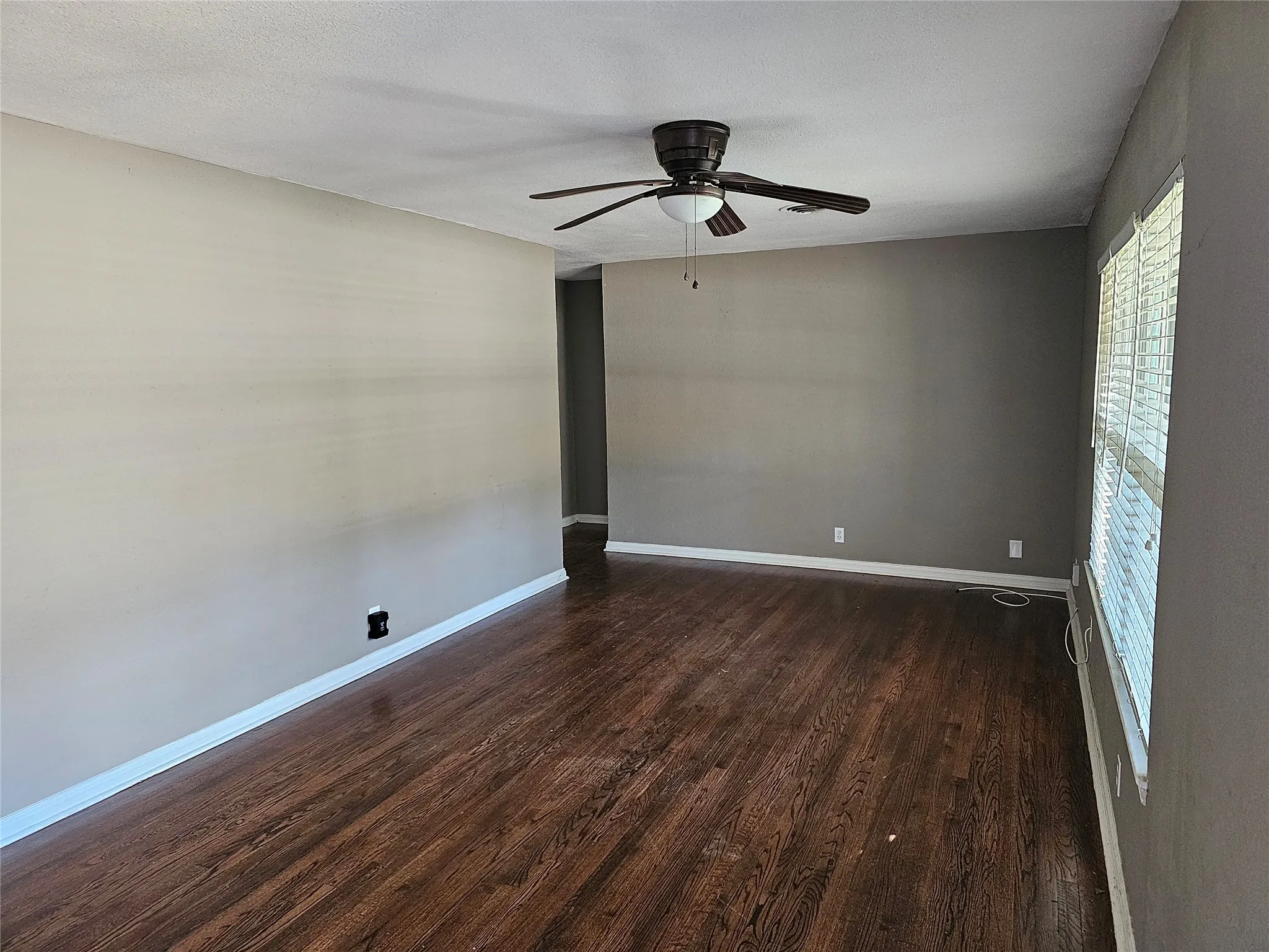 Spacious room featuring warm wood-finish flooring, neutral wall finishes, and ceiling-mounted fan with integrated lighting