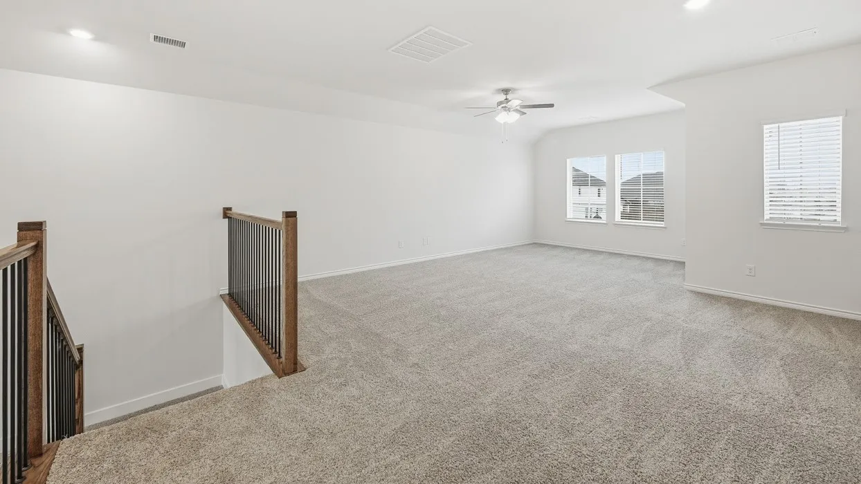 Spacious loft area featuring light-toned carpeting, ample natural light from multiple windows, and a ceiling fan