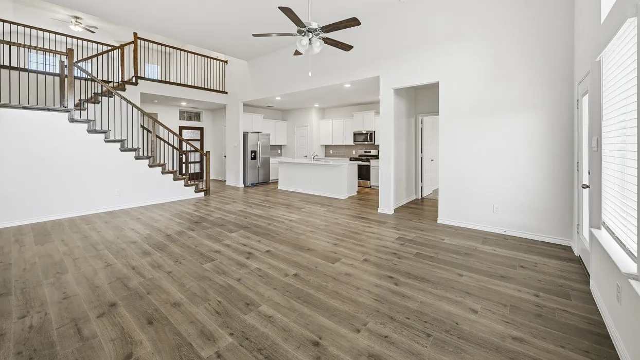 Spacious living area featuring wood-finish flooring, a soaring ceiling with a ceiling fan, and a prominent staircase with dark wood railings and black balusters
