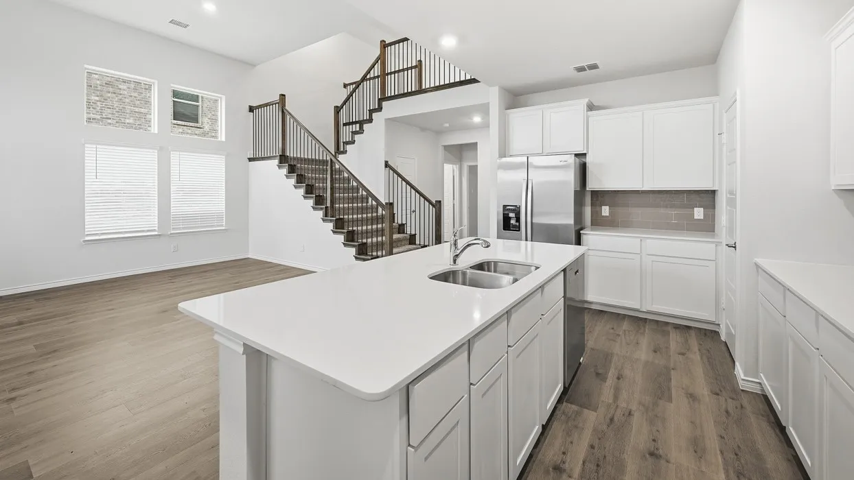 Spacious interior featuring a kitchen island with dual basin sink, stainless steel appliances, white cabinetry, and wood-finish flooring