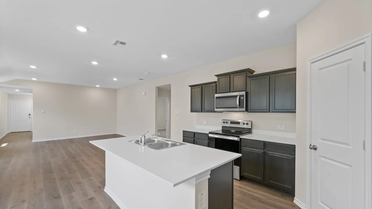 Open-concept kitchen and living area featuring dark wood-finish cabinetry, white countertops, stainless steel appliances, and wood-finish flooring