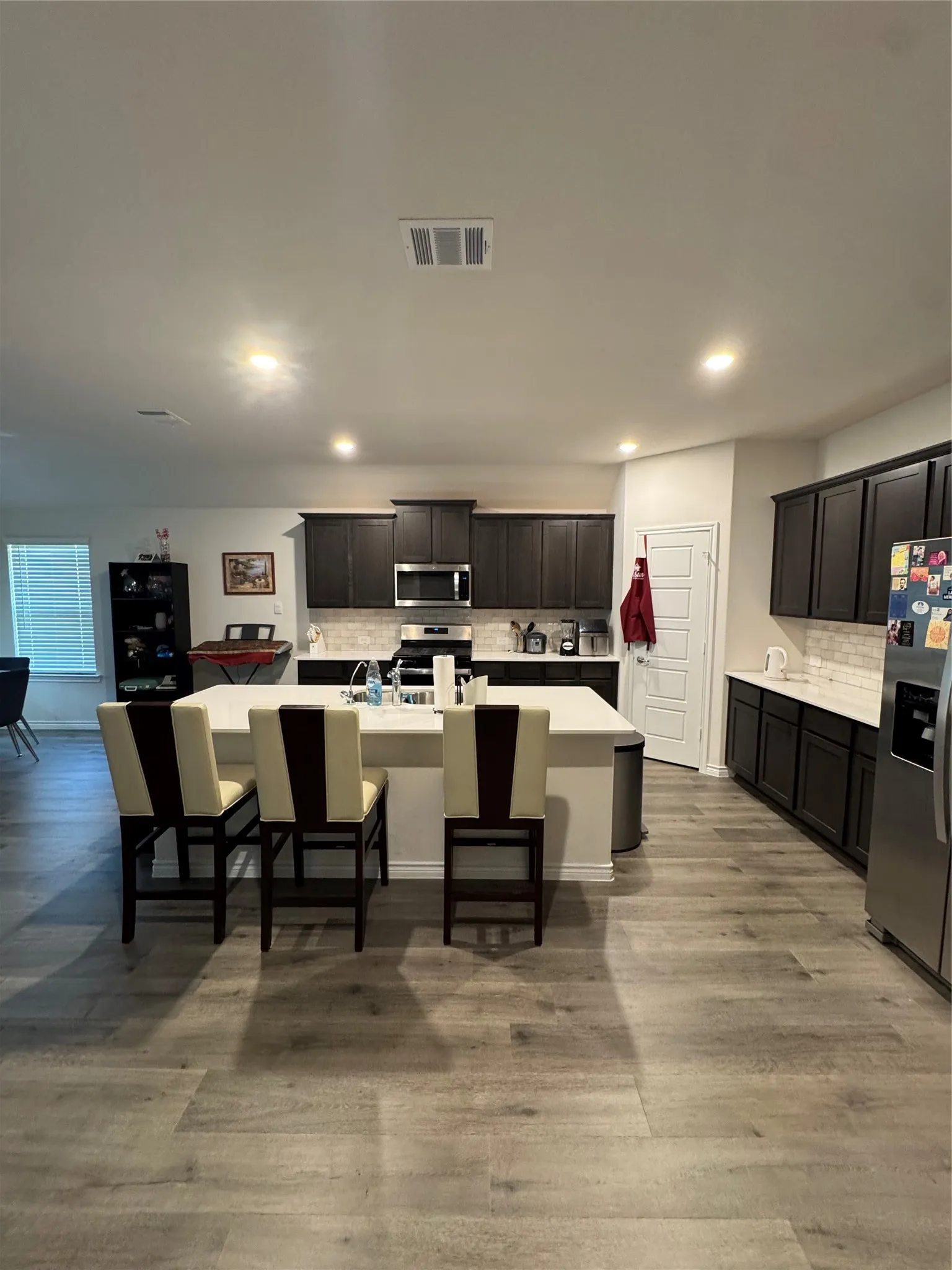 Kitchen featuring refrigerator, range, decorative backsplash, a kitchen island with sink, and light countertops