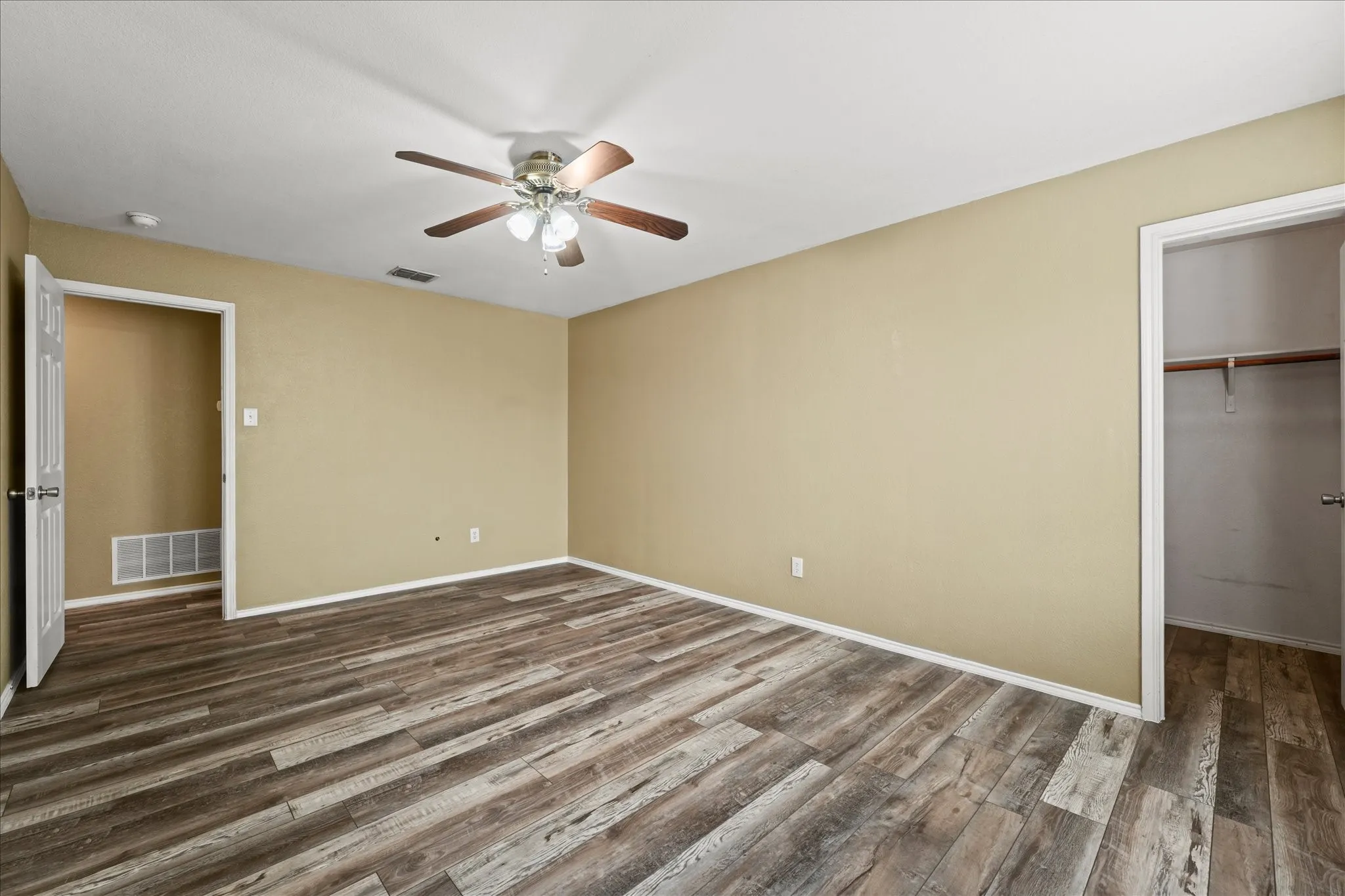 Unfurnished bedroom with dark wood-style flooring, a ceiling fan, a closet, and a walk in closet