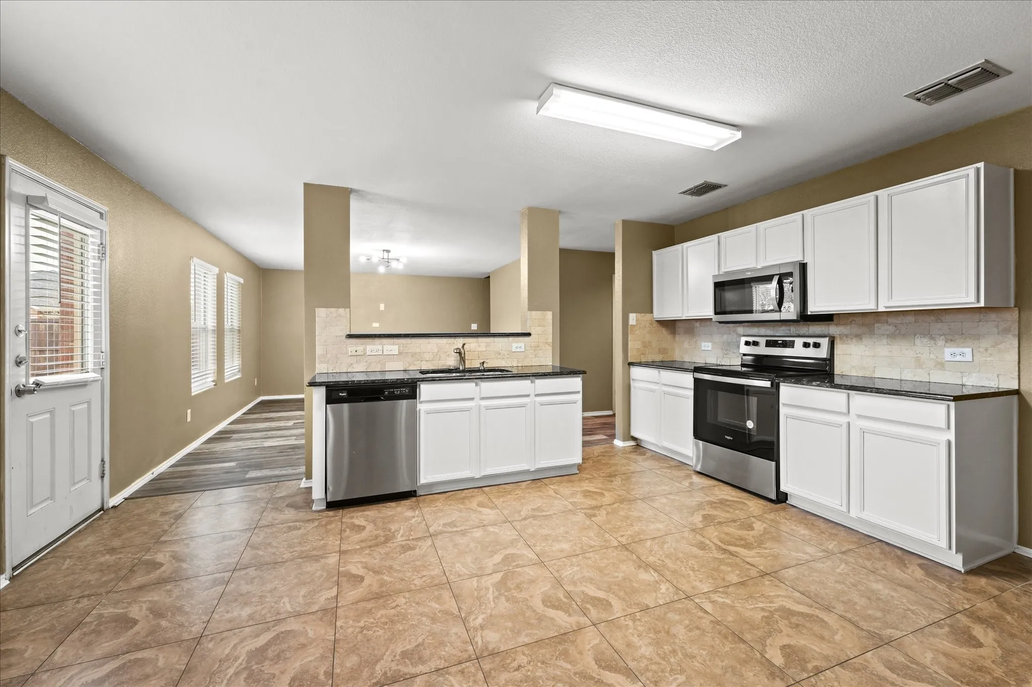 Kitchen with appliances with stainless steel finishes, dark countertops, tasteful backsplash, white cabinets, and a textured ceiling