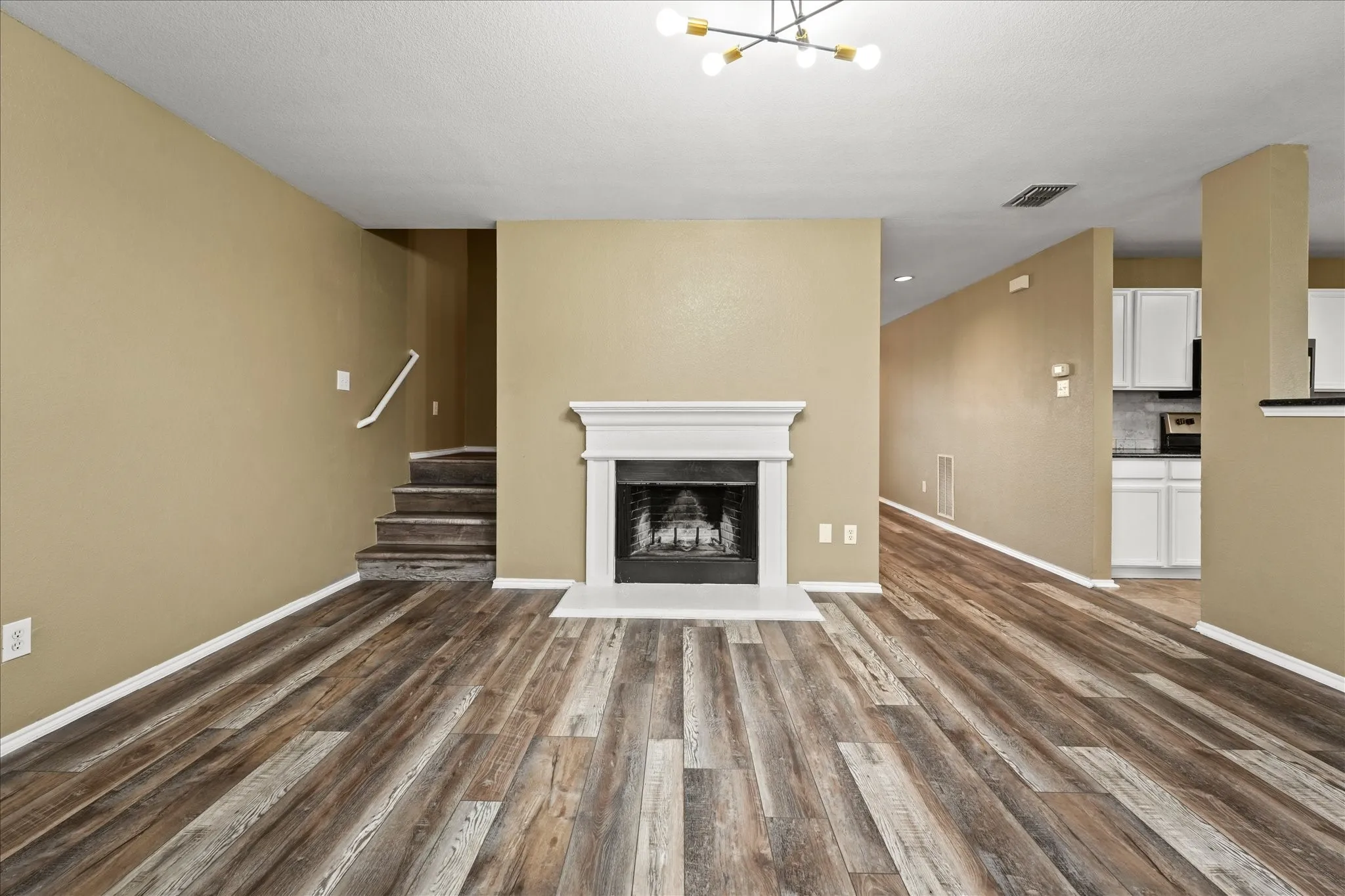 Unfurnished living room with dark wood-style floors, stairway, a chandelier, and a fireplace with raised hearth